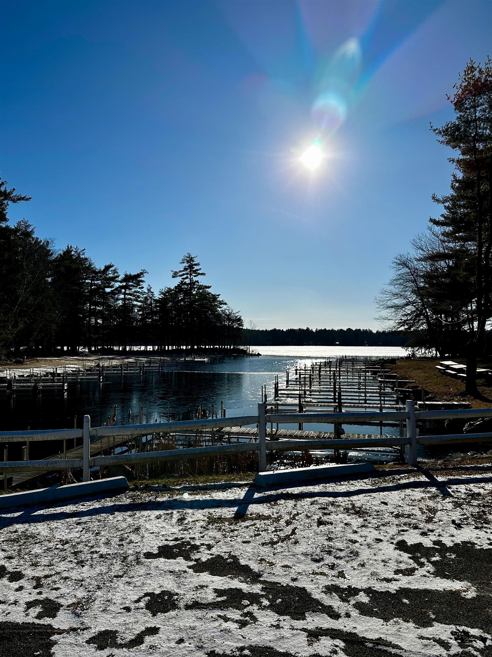 Lakeside marina with empty docks, a snow-covered shoreline, and bright winter sun.