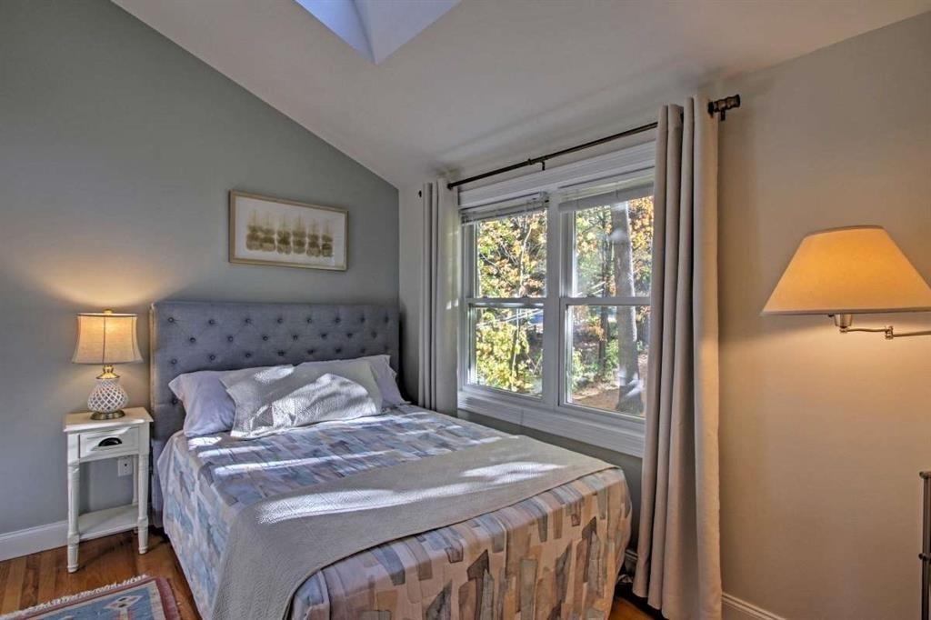 Bedroom with a gray tufted headboard and large window overlooking autumn trees.