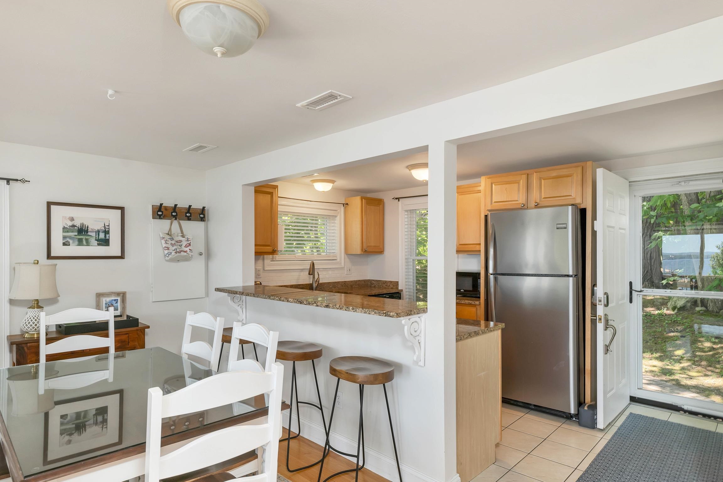 Kitchen and dining area with a granite breakfast bar, stainless-steel refrigerator, and open door overlooking water.