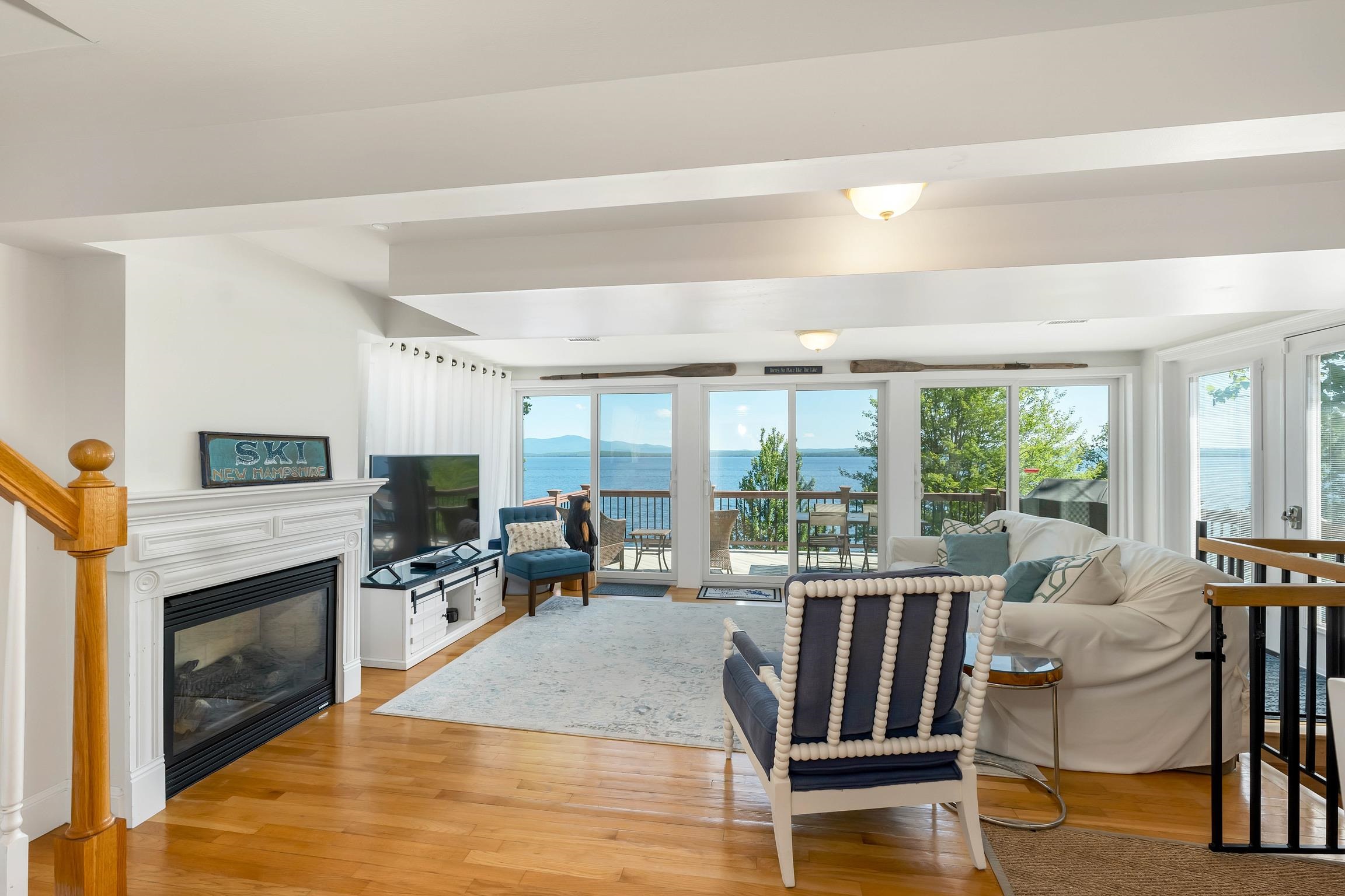 Living room with a fireplace, white seating, and wide lake views through glass doors.