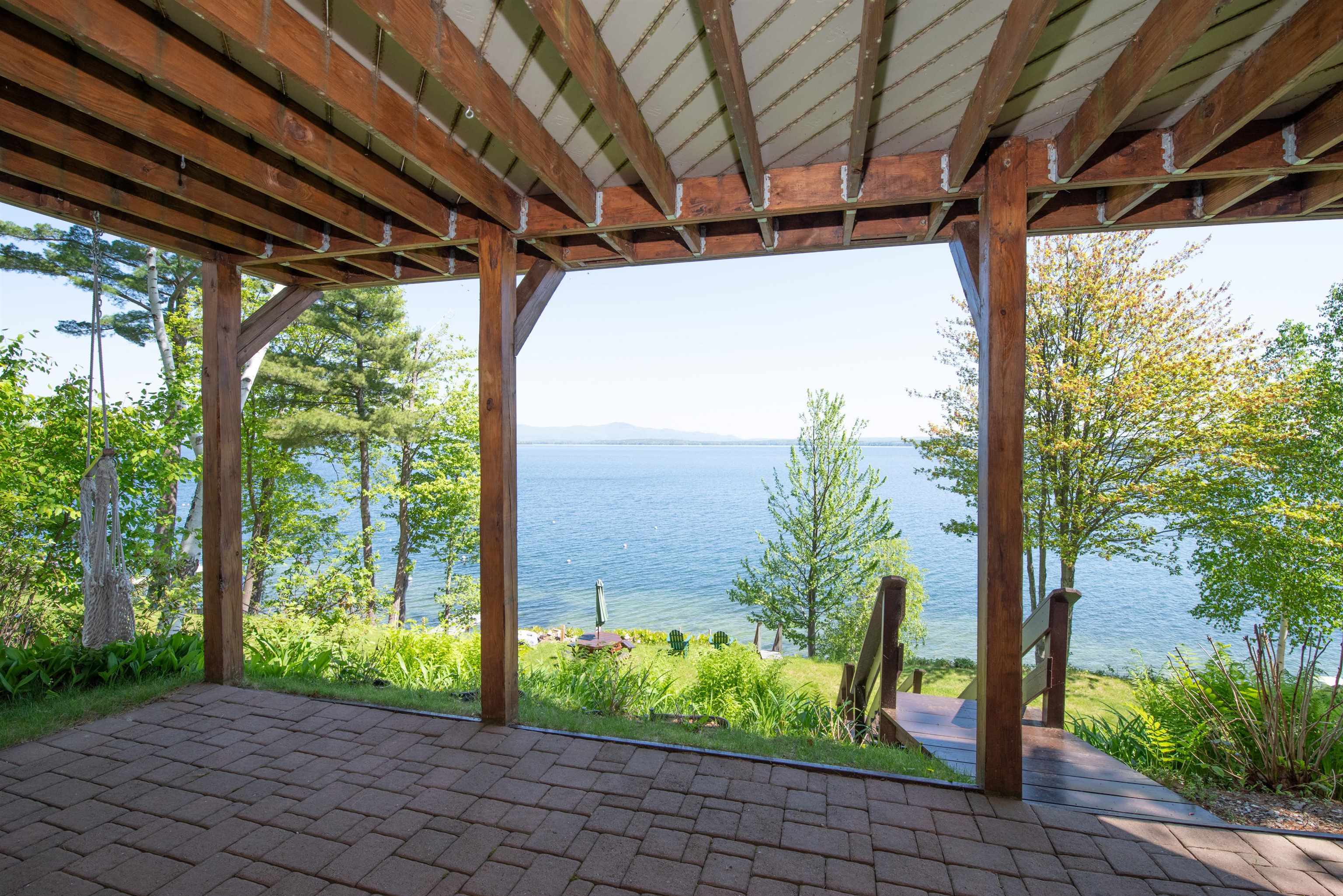 Covered timber patio overlooking a lake, with steps leading down toward the shore.