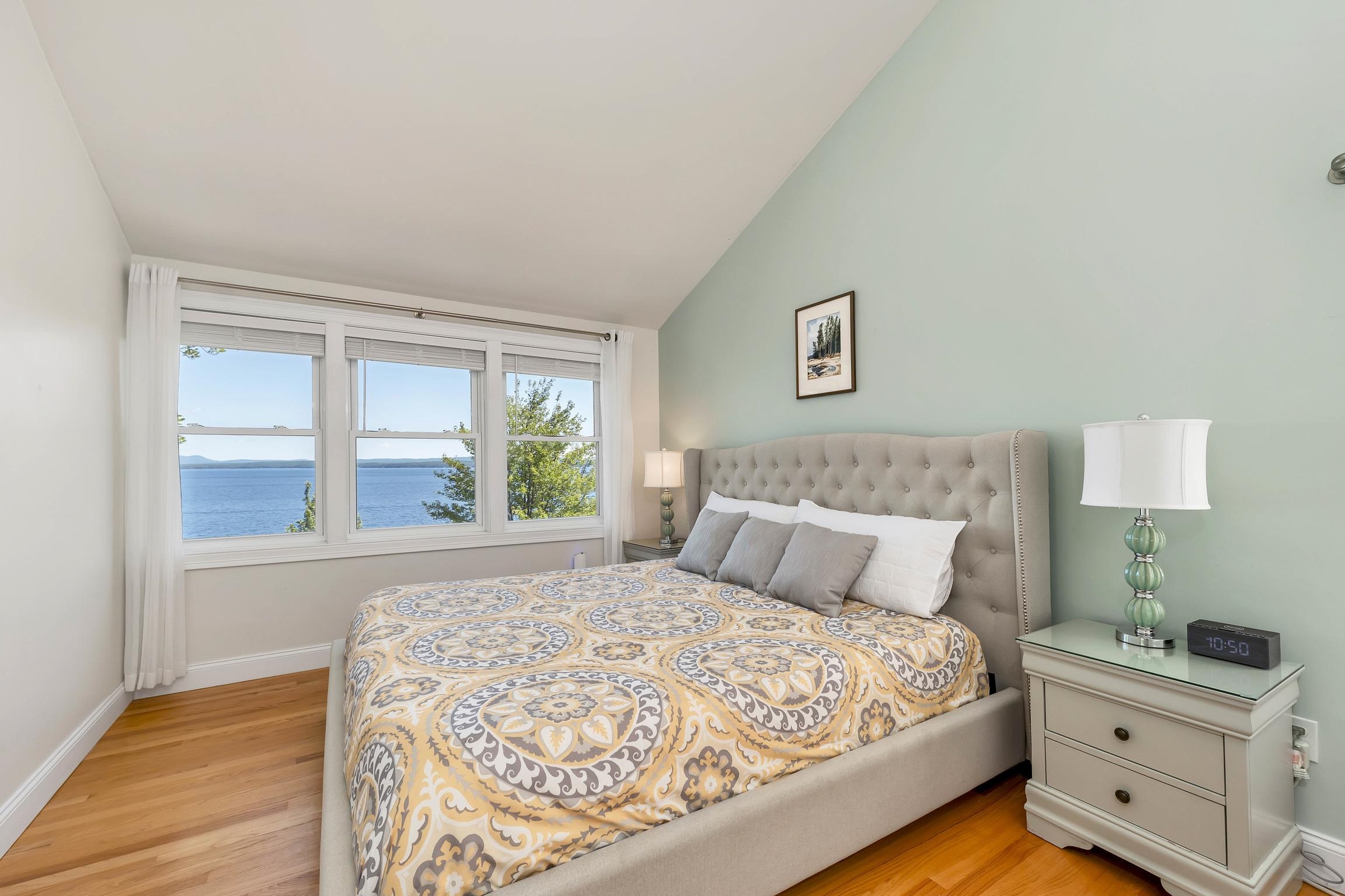 Furnished bedroom with a lake view through three windows and a patterned bedspread.