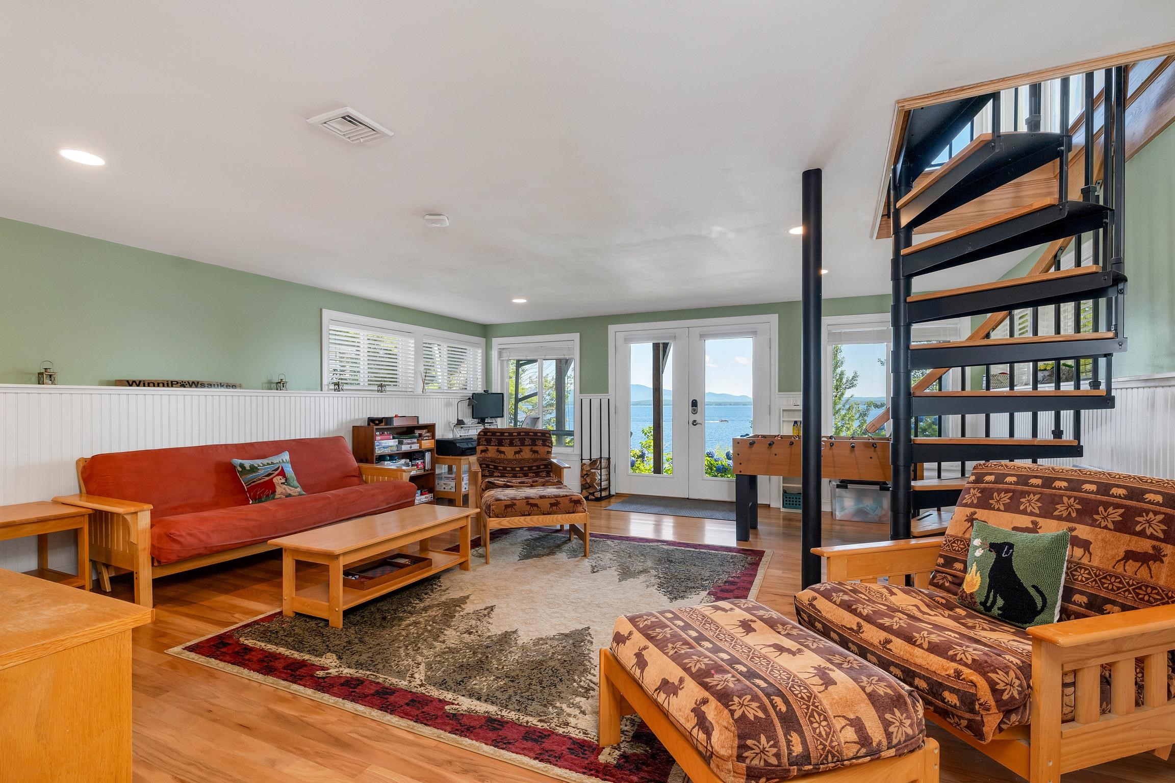 Living room with a spiral staircase, patterned chairs, and lake views through glass doors.