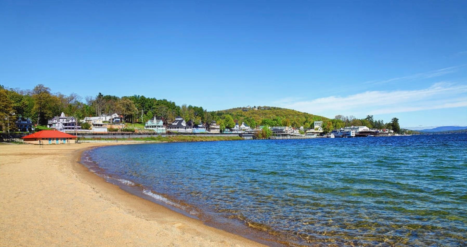 Sandy lakeside beach curving toward shoreline homes and autumn-colored trees.