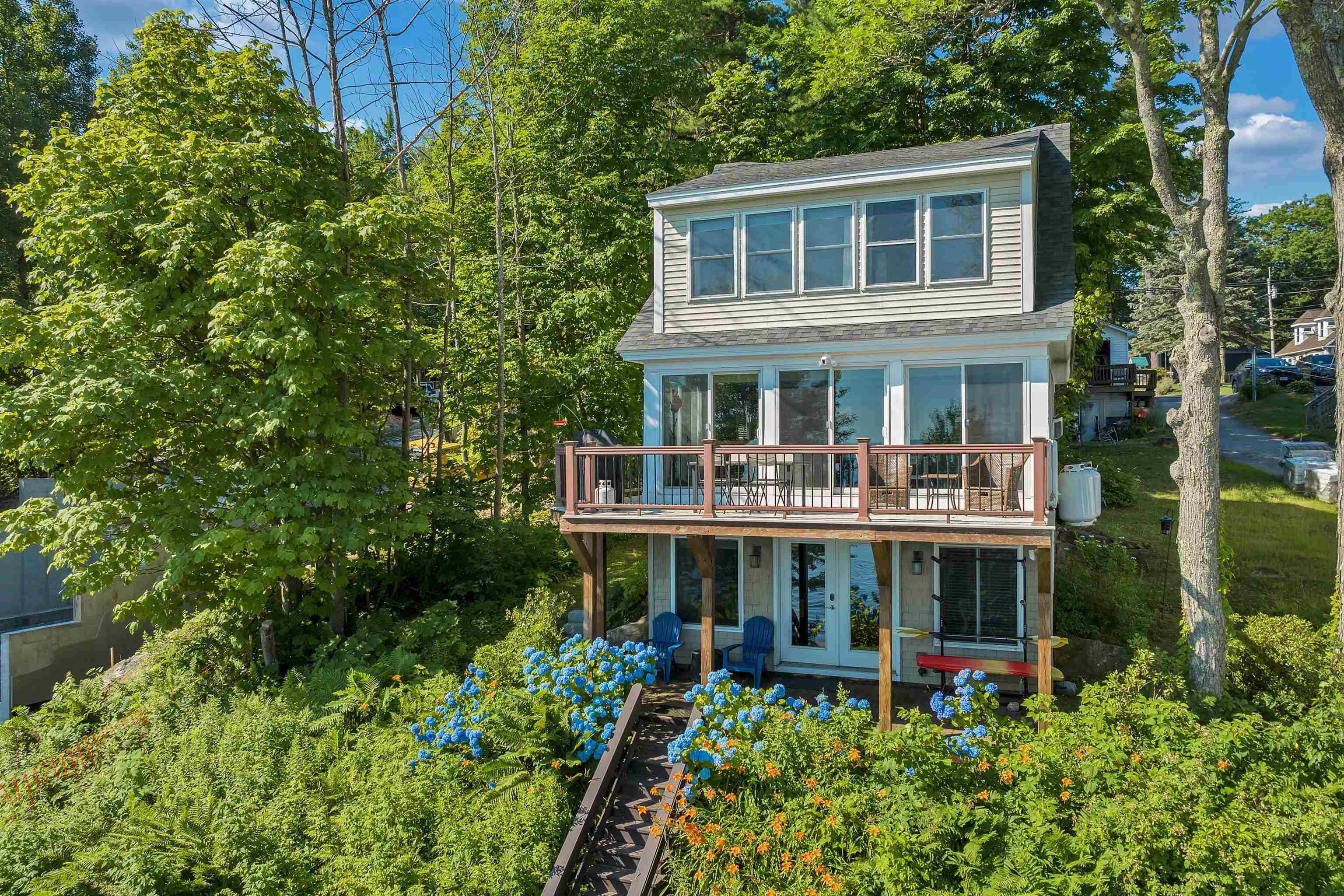 Lakeside home with a raised deck, large windows, and a flower-lined garden path.