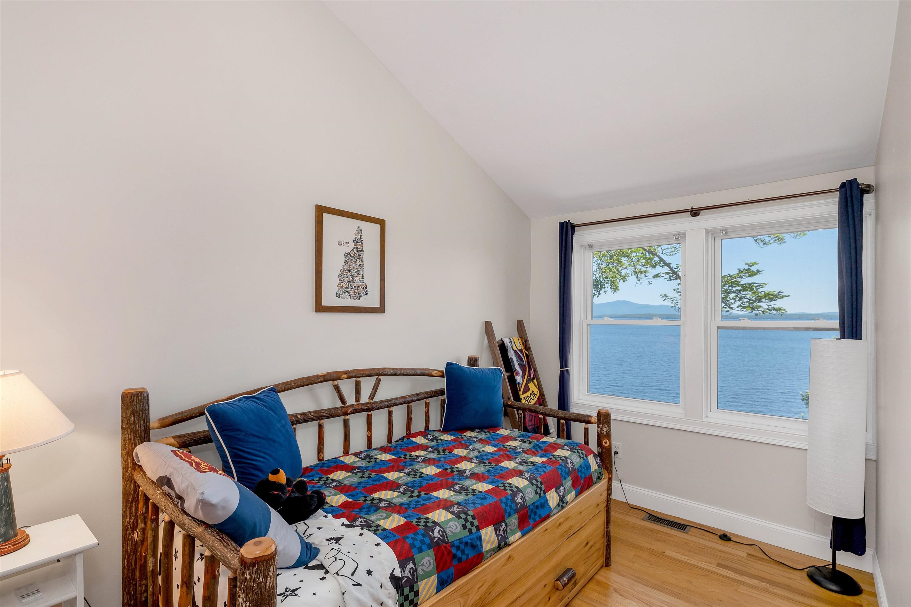 Bedroom with a rustic wooden daybed and colorful quilt overlooking a lake.