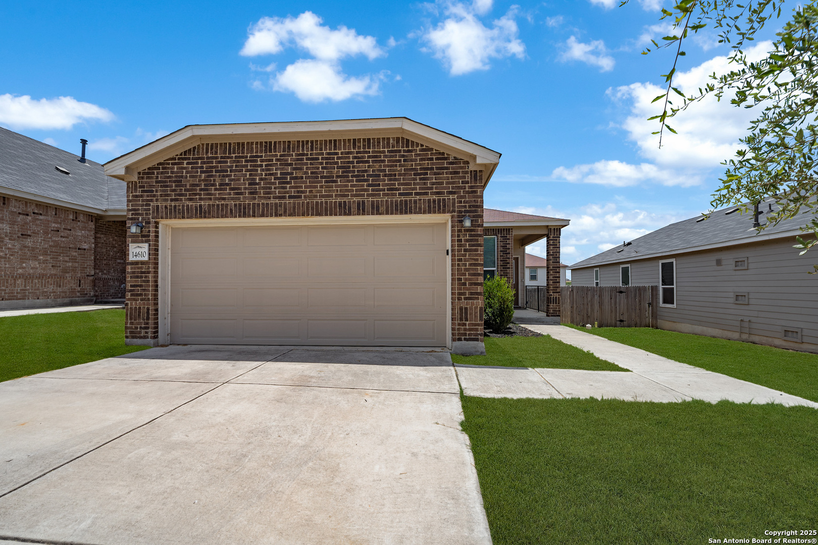 Brick home with a wide double garage door, concrete driveway, and green lawn.