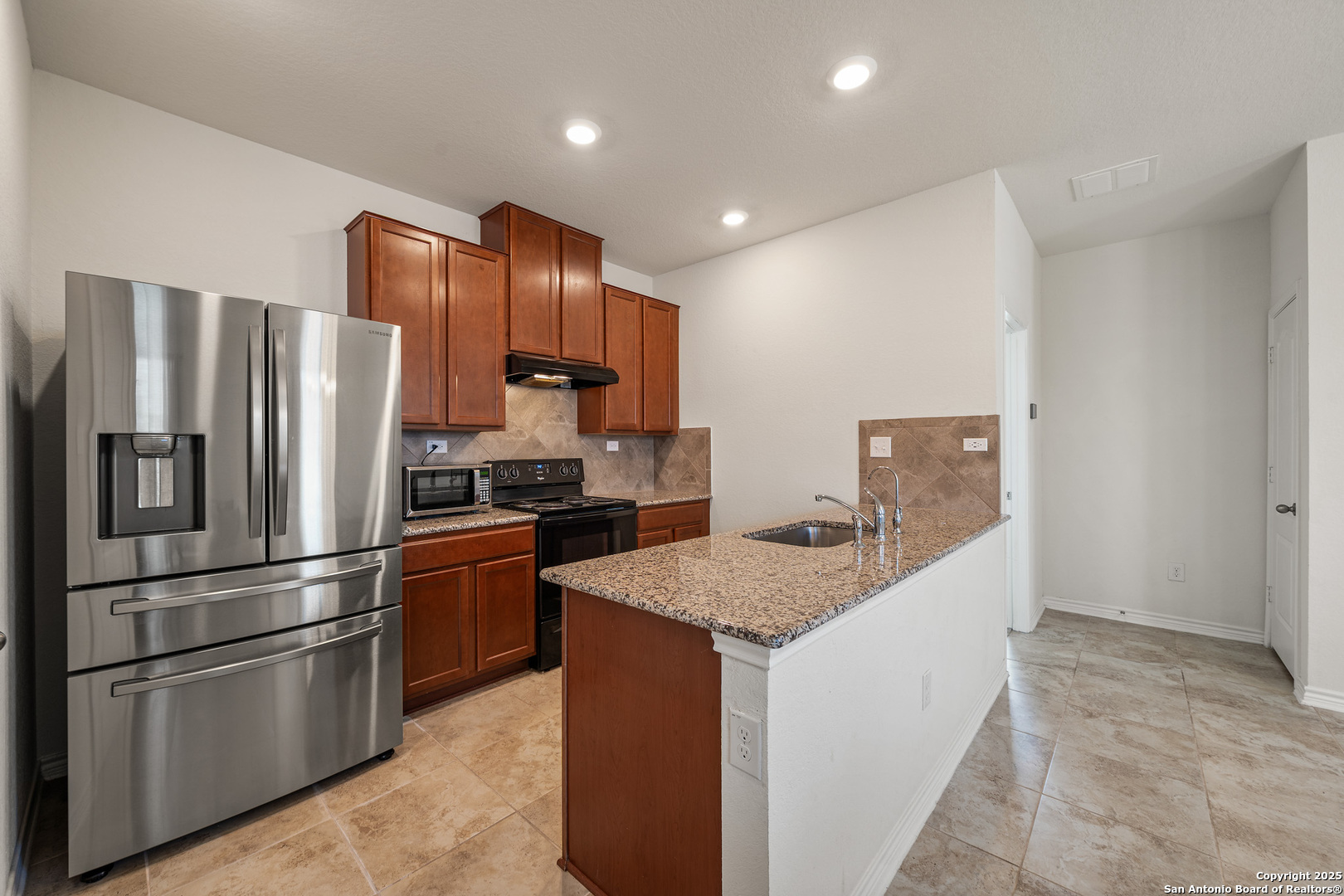 Kitchen with cherry cabinets, granite island sink, stainless steel refrigerator, and tiled floors.