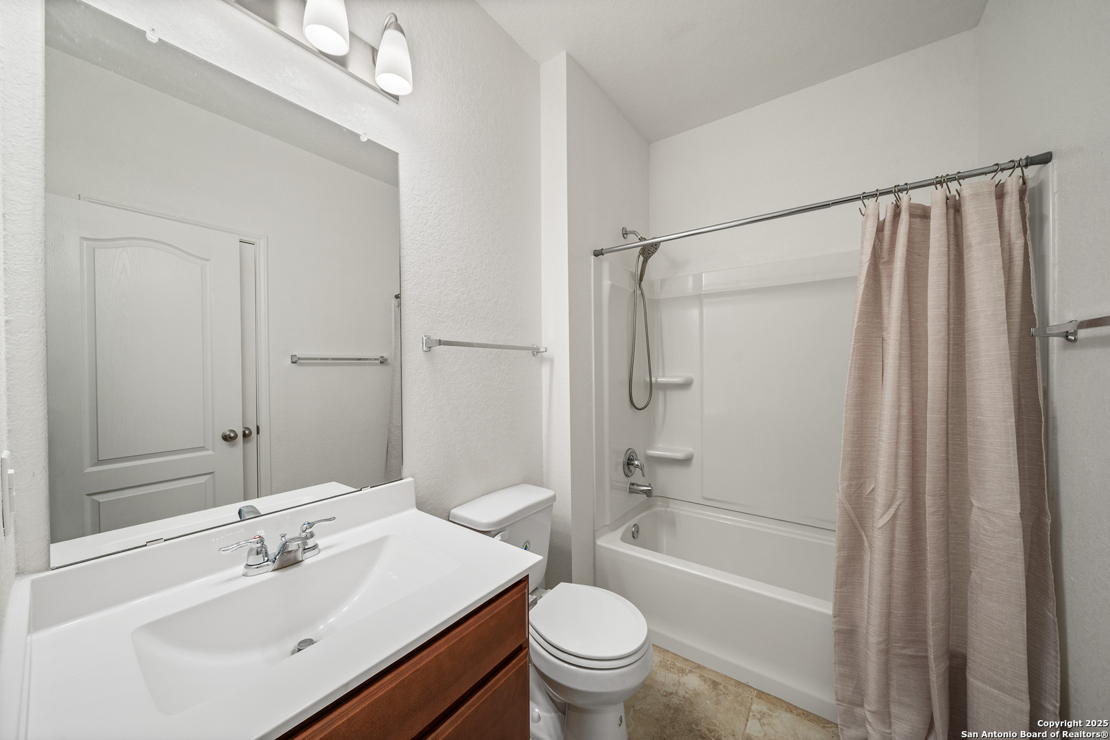 Bathroom with a white tub and shower, beige curtain, and dark wood vanity.