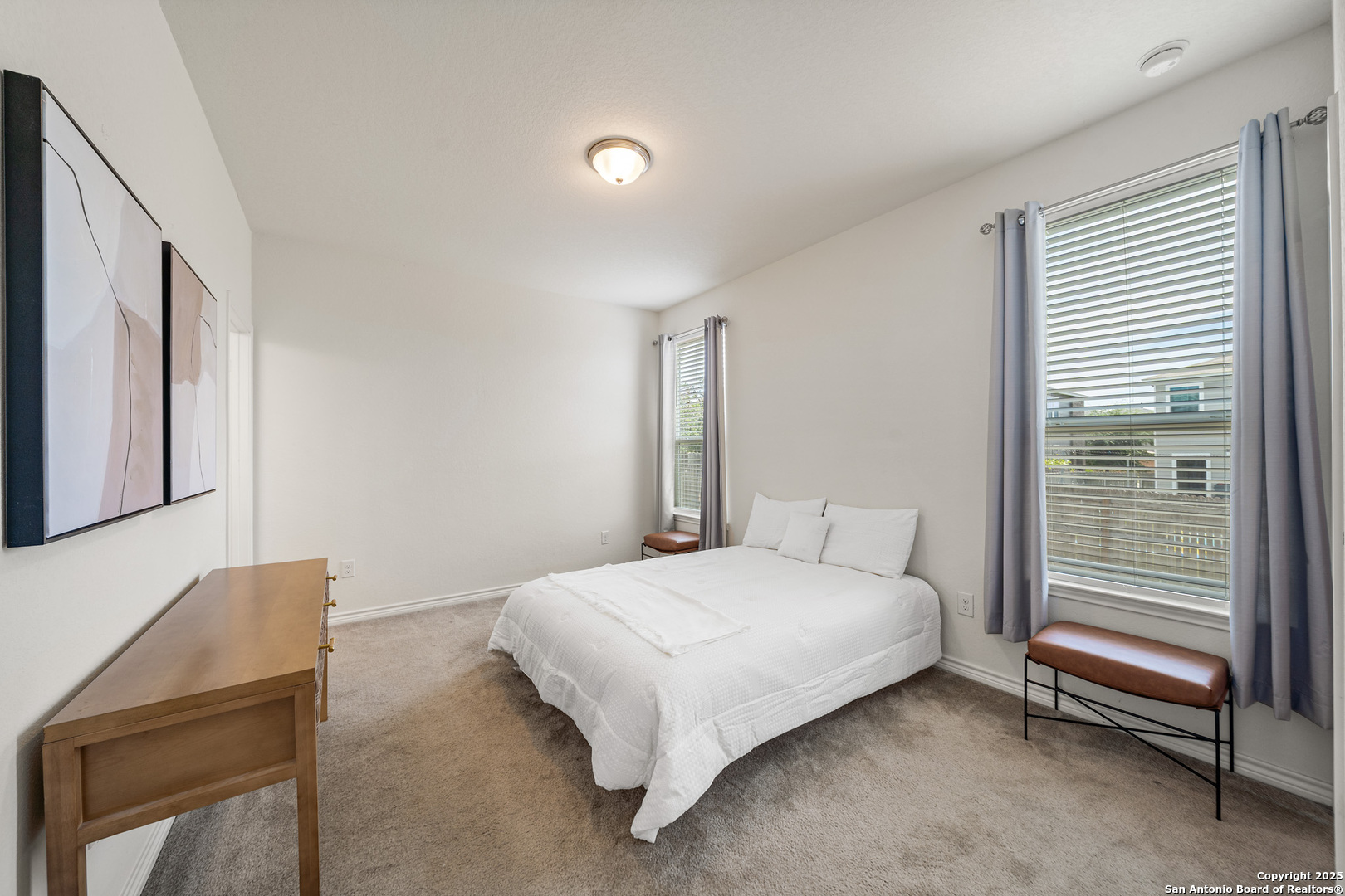 Staged bedroom with a white bed, two curtained windows, and a wooden dresser.
