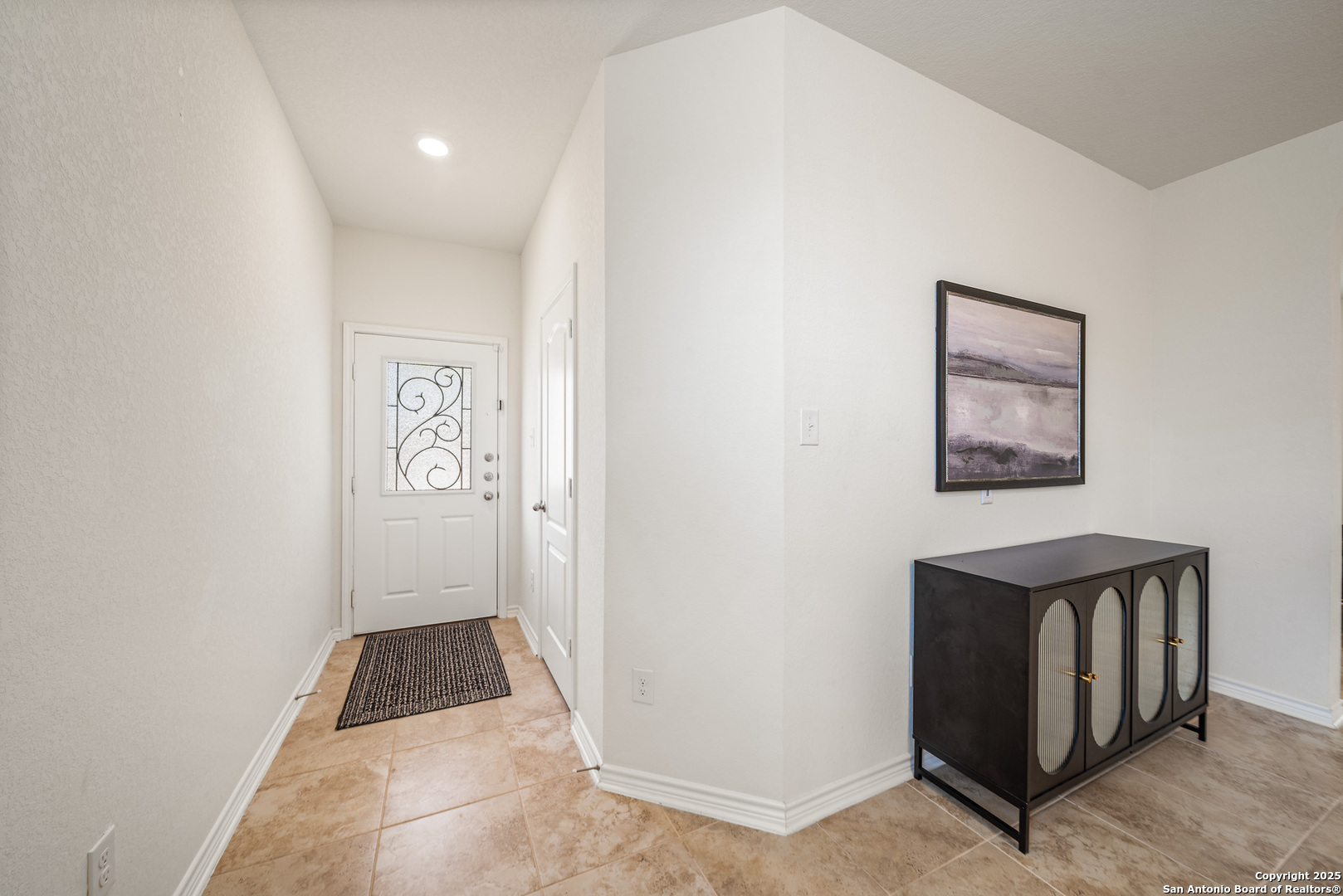 Entry foyer with tan tile, a decorative-glass front door, and a dark console cabinet.