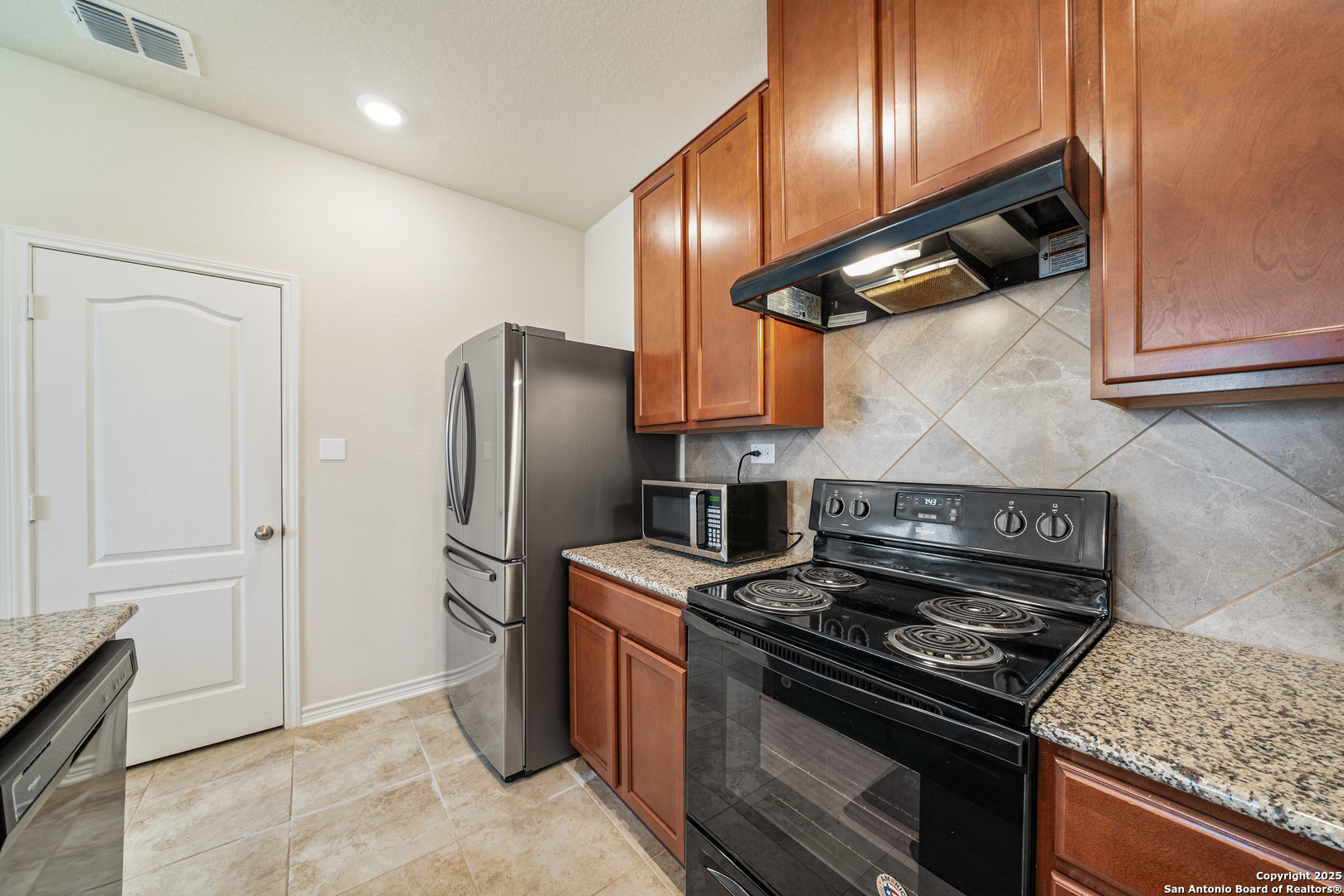 Kitchen with wood cabinets, granite countertops, stainless refrigerator, and black electric range.