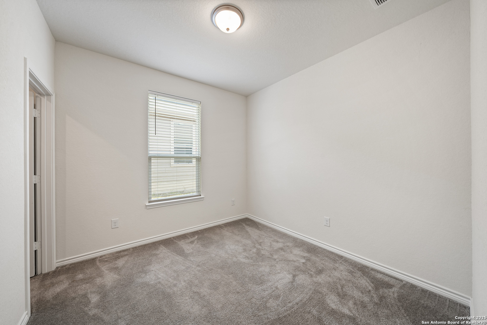 Empty bedroom with gray carpet and a window fitted with blinds.