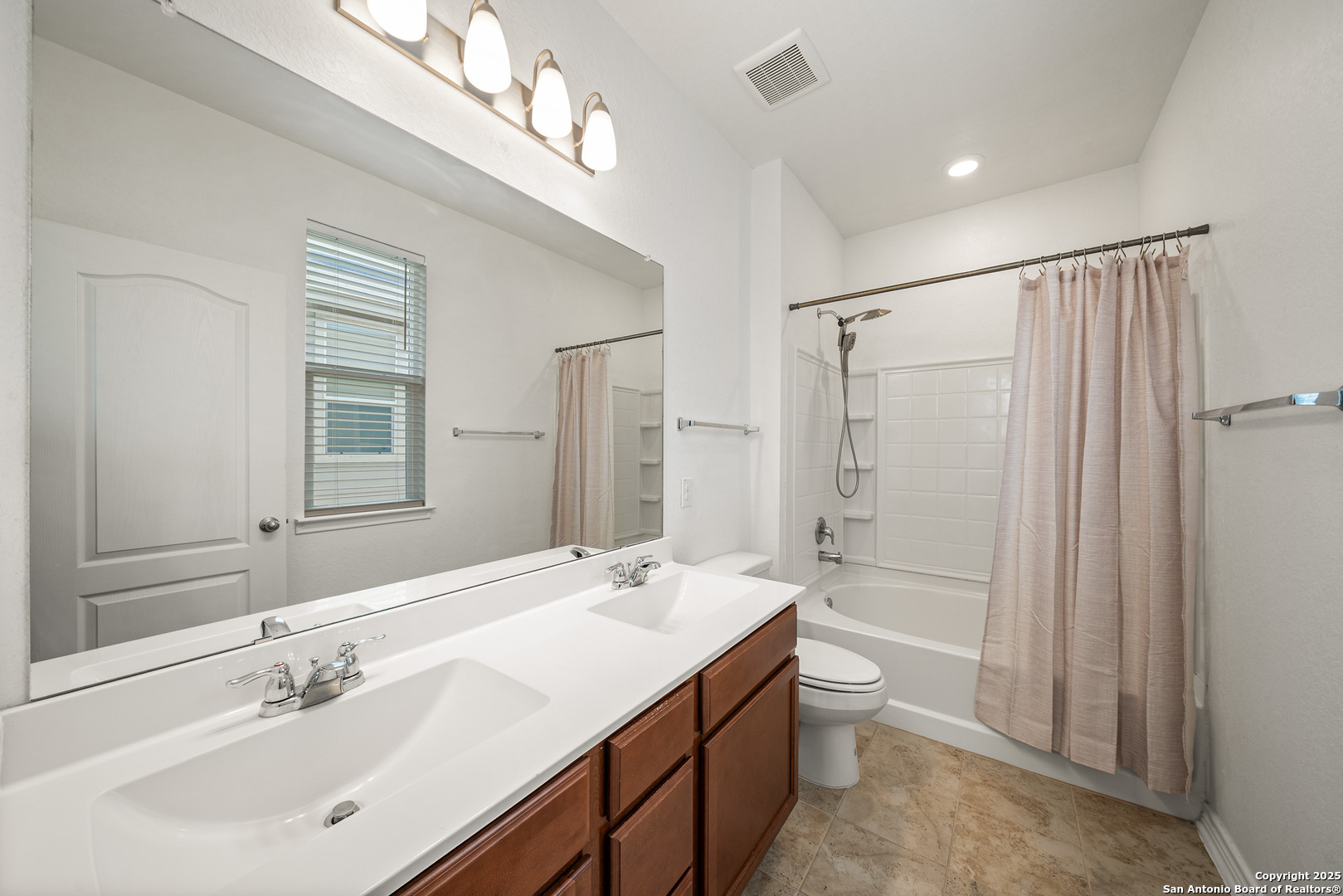Bathroom with a double-sink vanity, dark wood cabinets, and a curtained tub-shower.