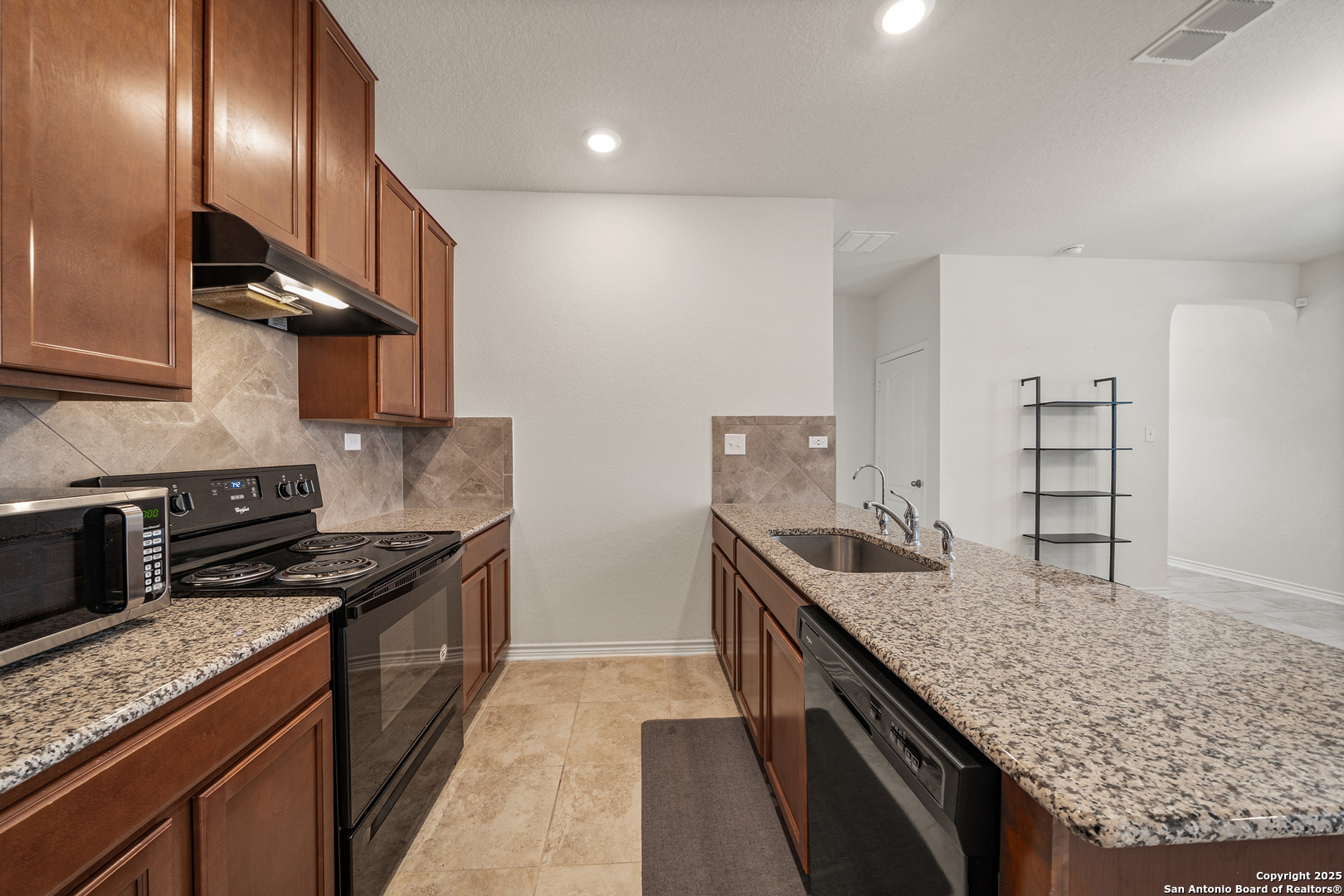 Kitchen with wood cabinets, granite counters, black appliances, and a long island with a double-basin sink.