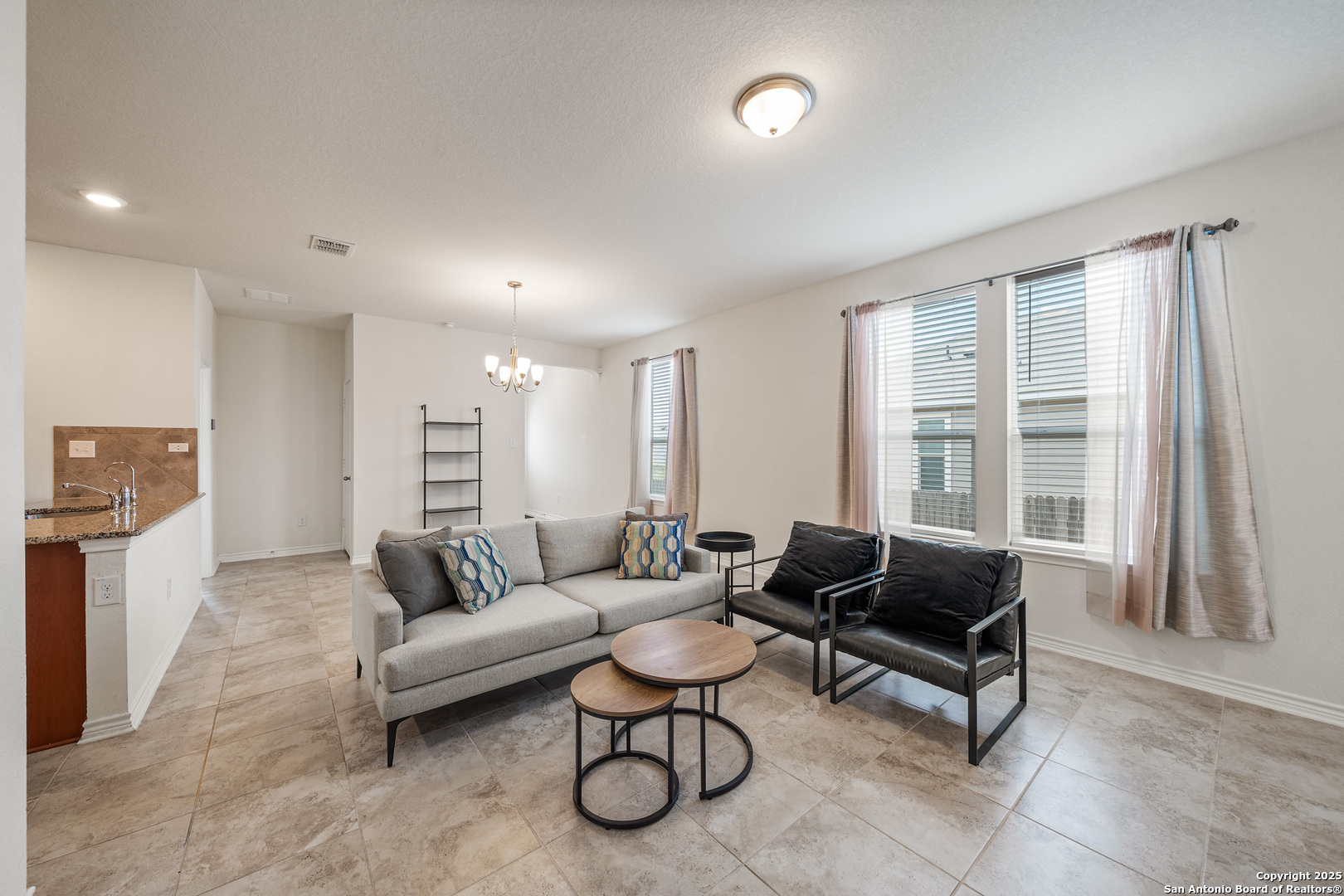 Furnished living room with a gray sofa, black armchairs, and large curtained windows.