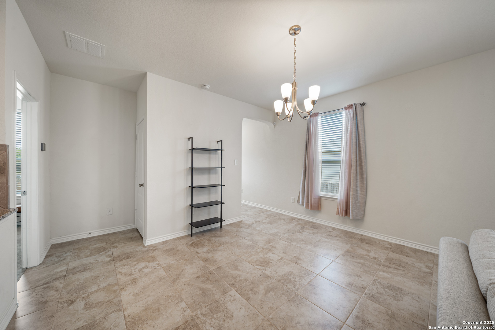 Dining area with beige tile floors, a brass chandelier, and a curtained window.