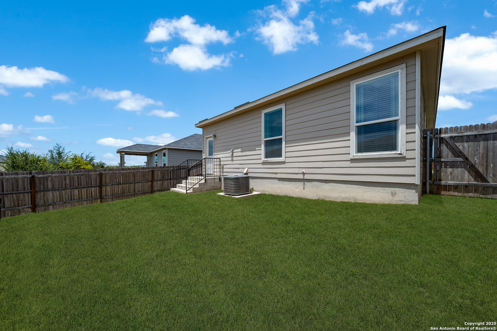 House’s rear exterior with a fenced grassy backyard and visible air-conditioning unit.