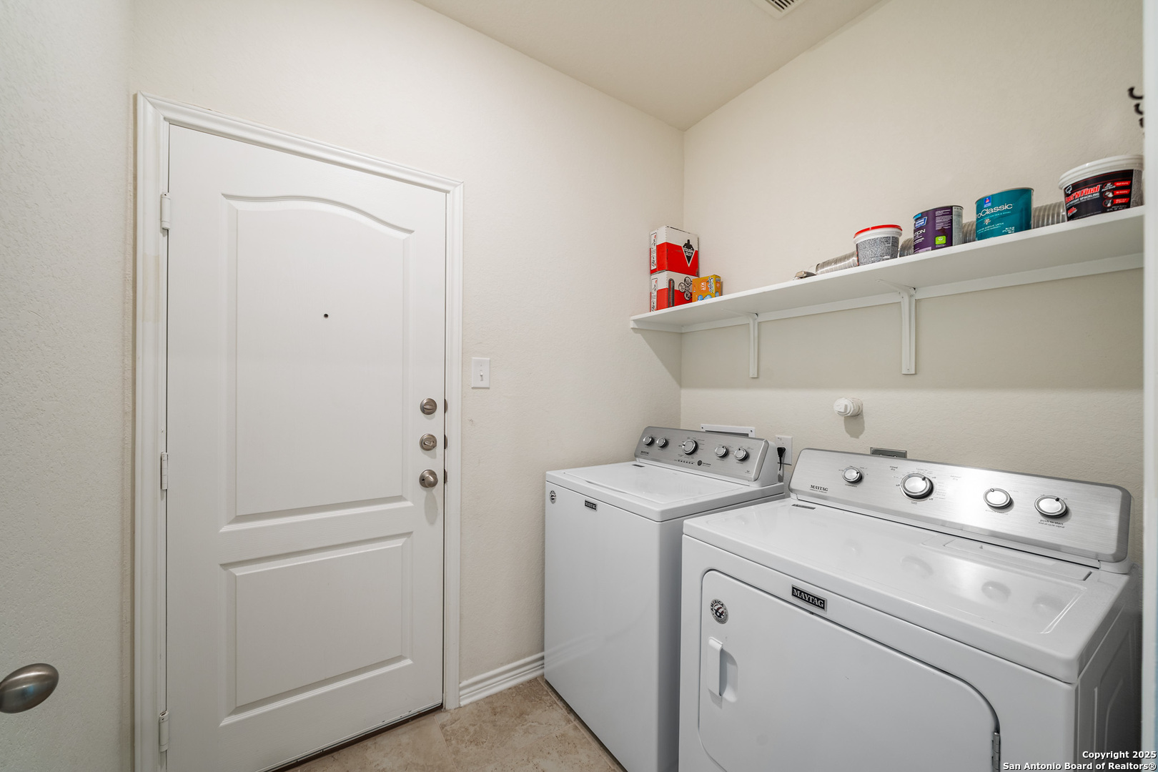 Laundry room with a white washer and dryer beneath a shelf.