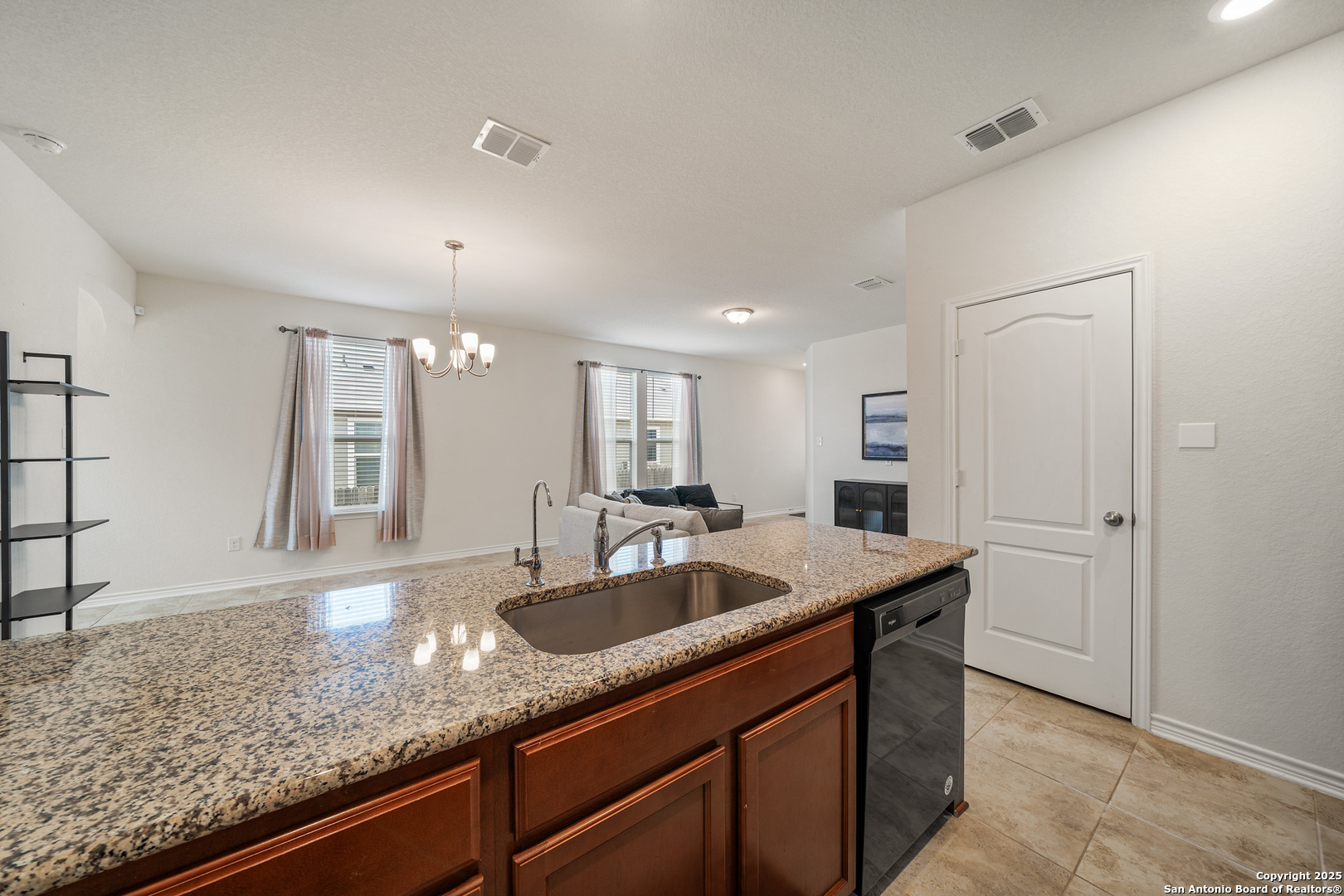 Kitchen island with speckled granite counters and sink overlooks a living room with a sofa and fireplace.