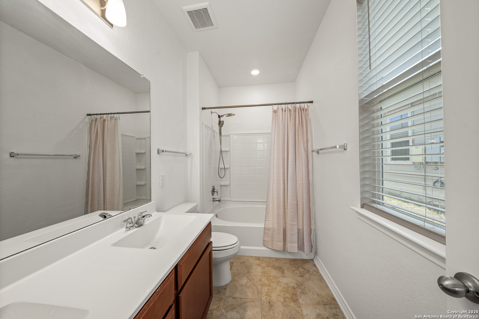 Bathroom with a wood vanity, large mirror, tub-shower, pale curtain, and window with blinds.