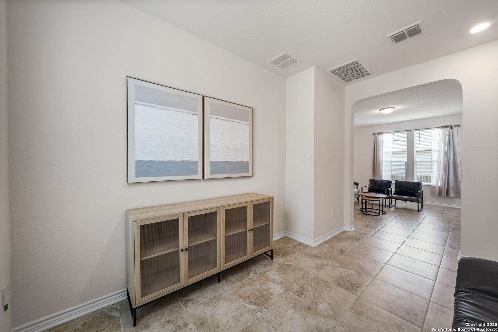 Furnished entry hall with tan tile floors, a wood console, and an arched opening to a sitting area.