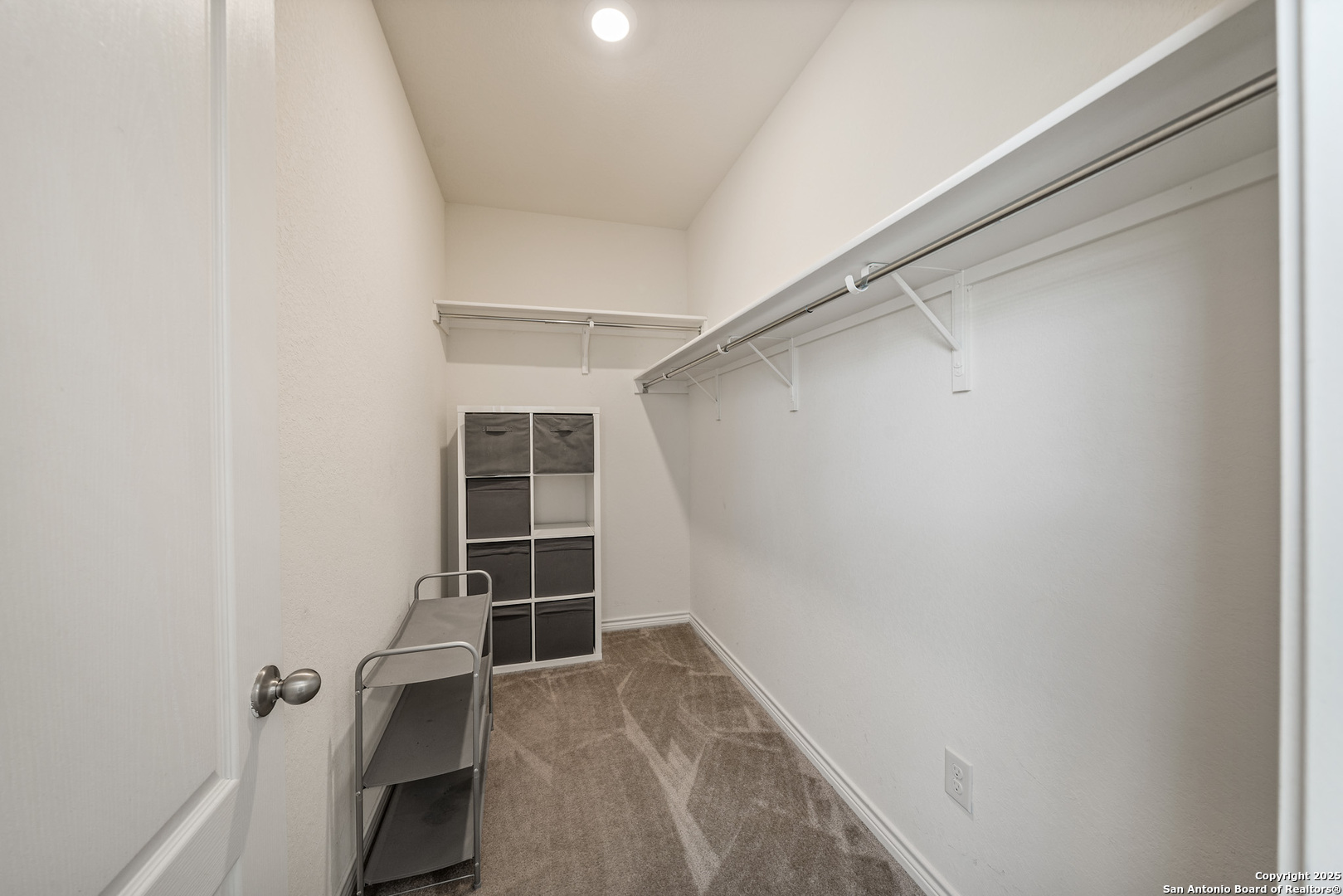 Walk-in closet with long hanging shelves, carpet, and storage drawers.