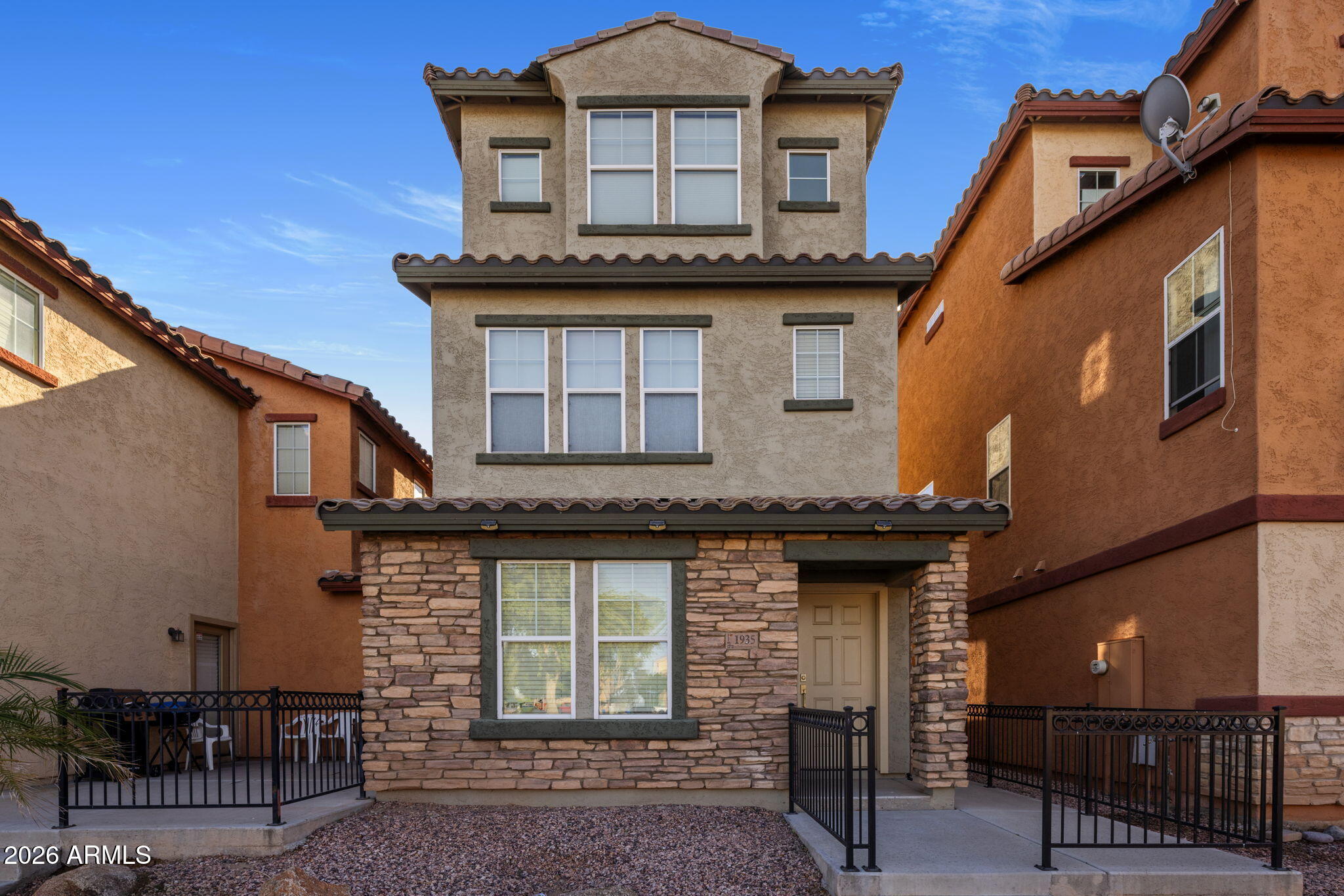 Three-story beige stucco home with a stone facade and gated front entry.