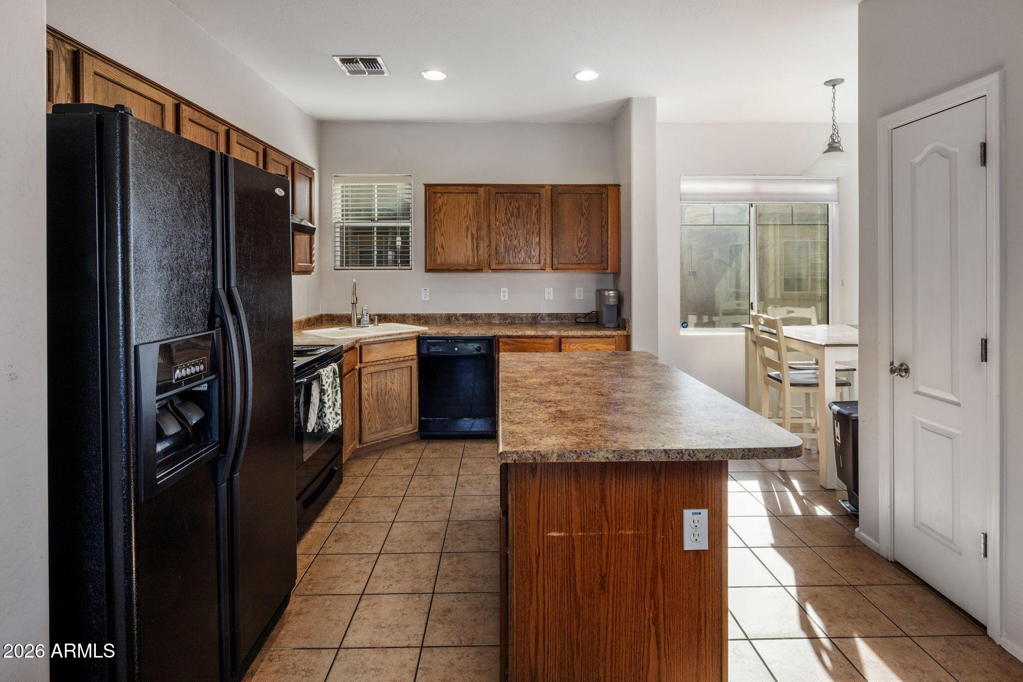 Kitchen with wood cabinets, black appliances, and a large central island beside a sunlit dining area.