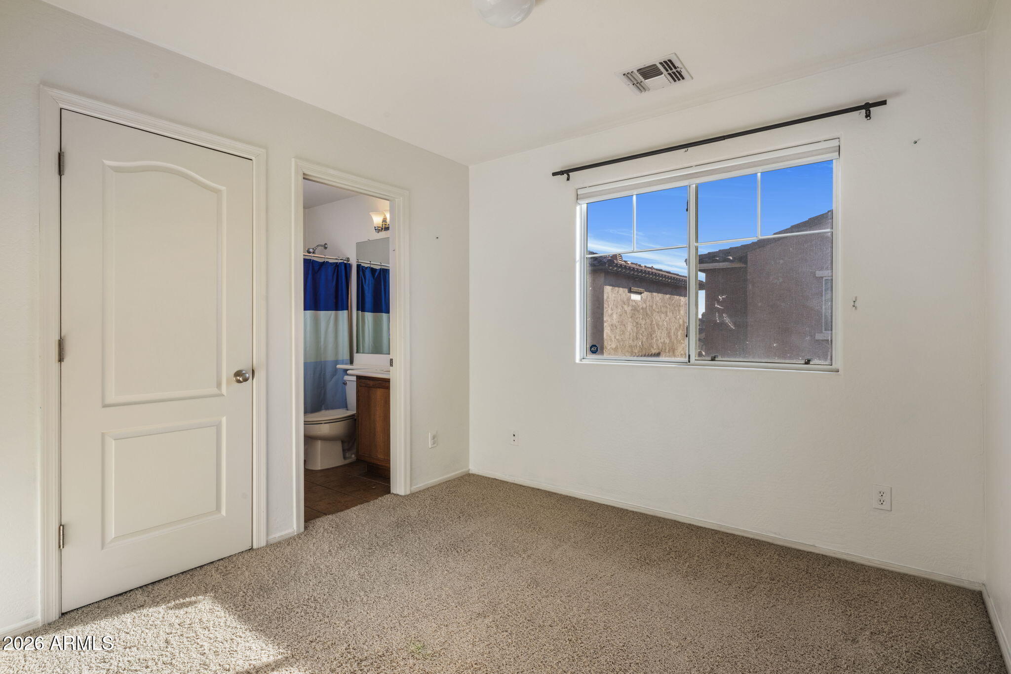 Empty carpeted bedroom with a large window and an open doorway to the bathroom.