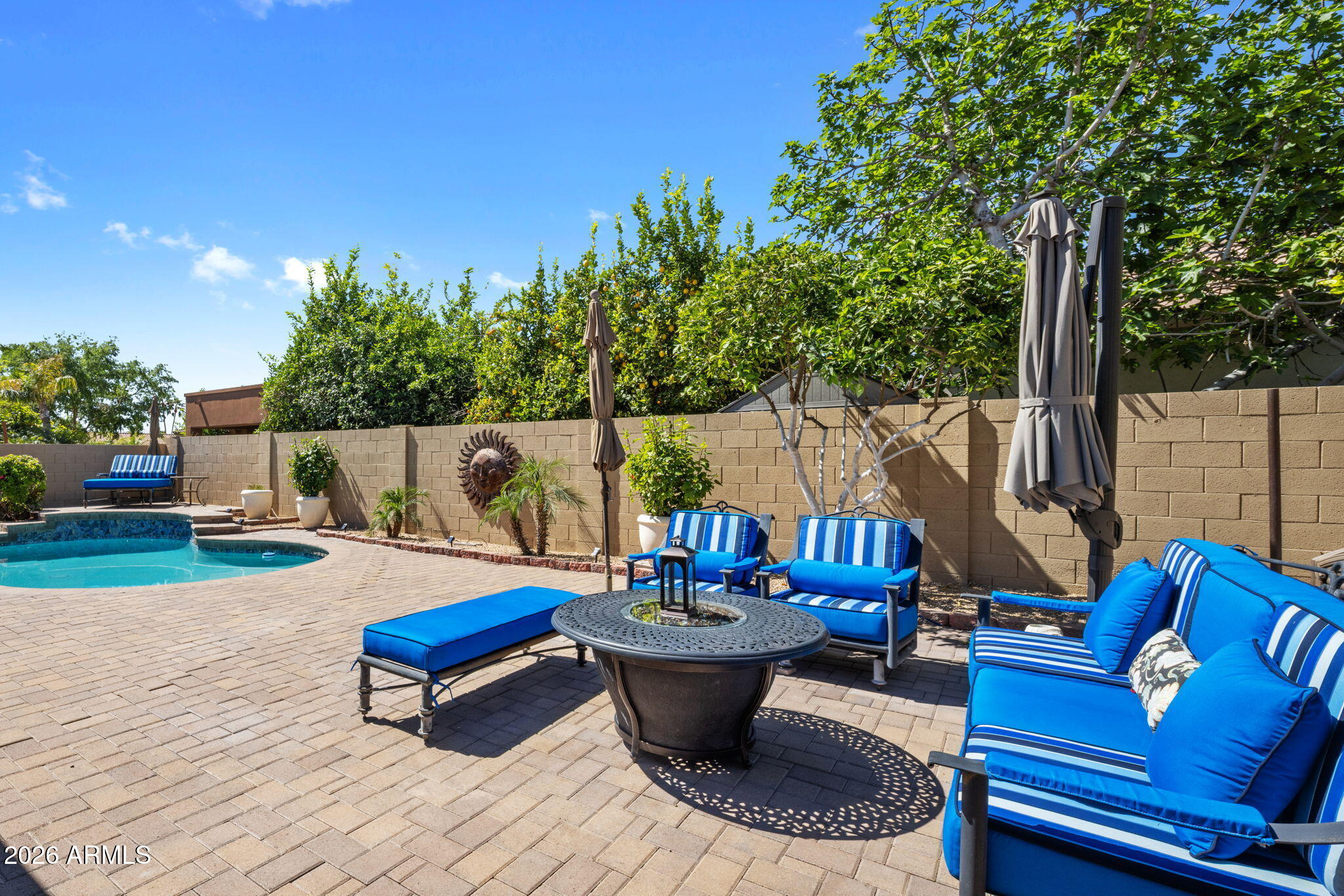 Backyard pool beside a paved patio with bright blue lounge seating and a round fire table.