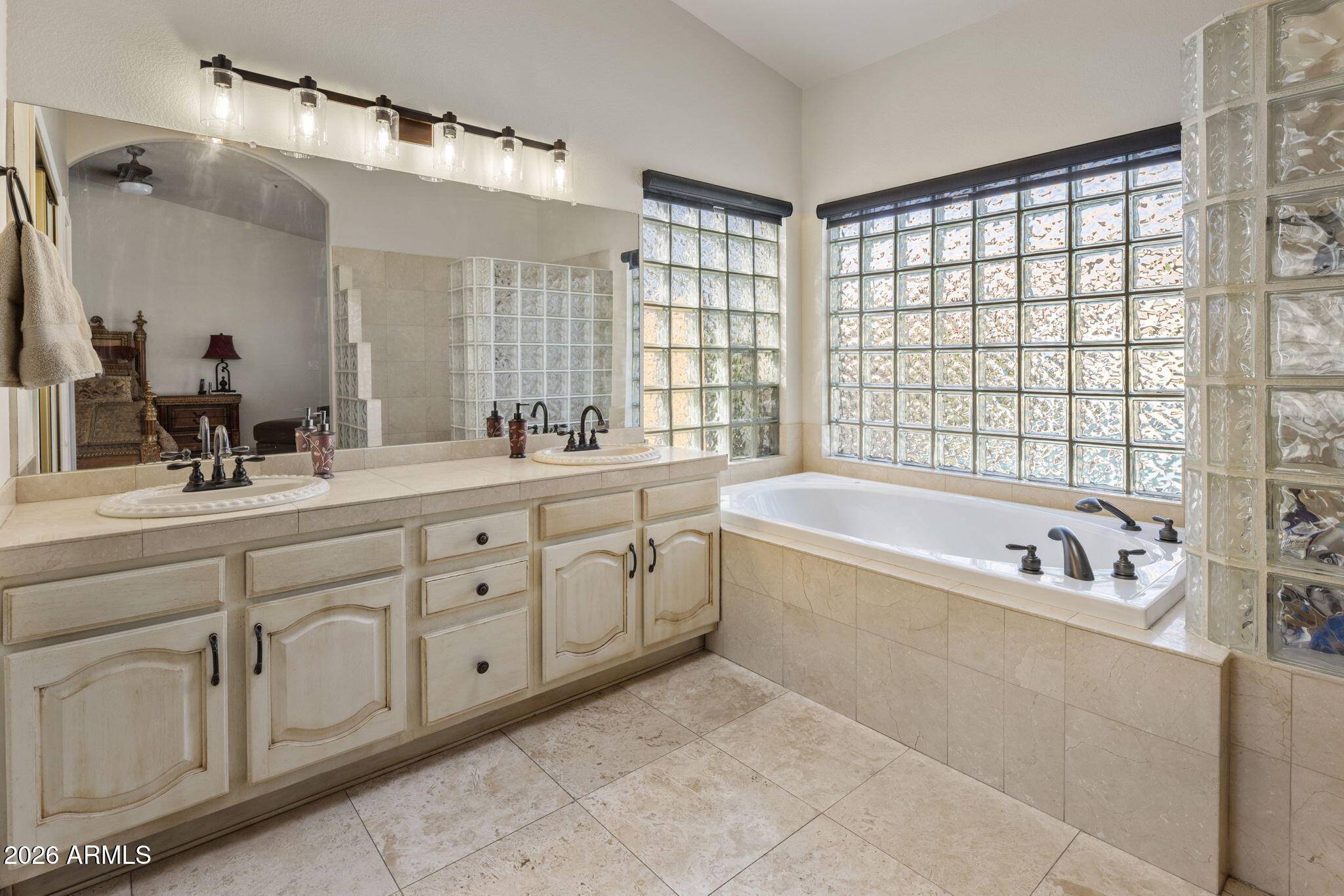Primary bathroom with a double vanity and soaking tub beneath large glass block windows.