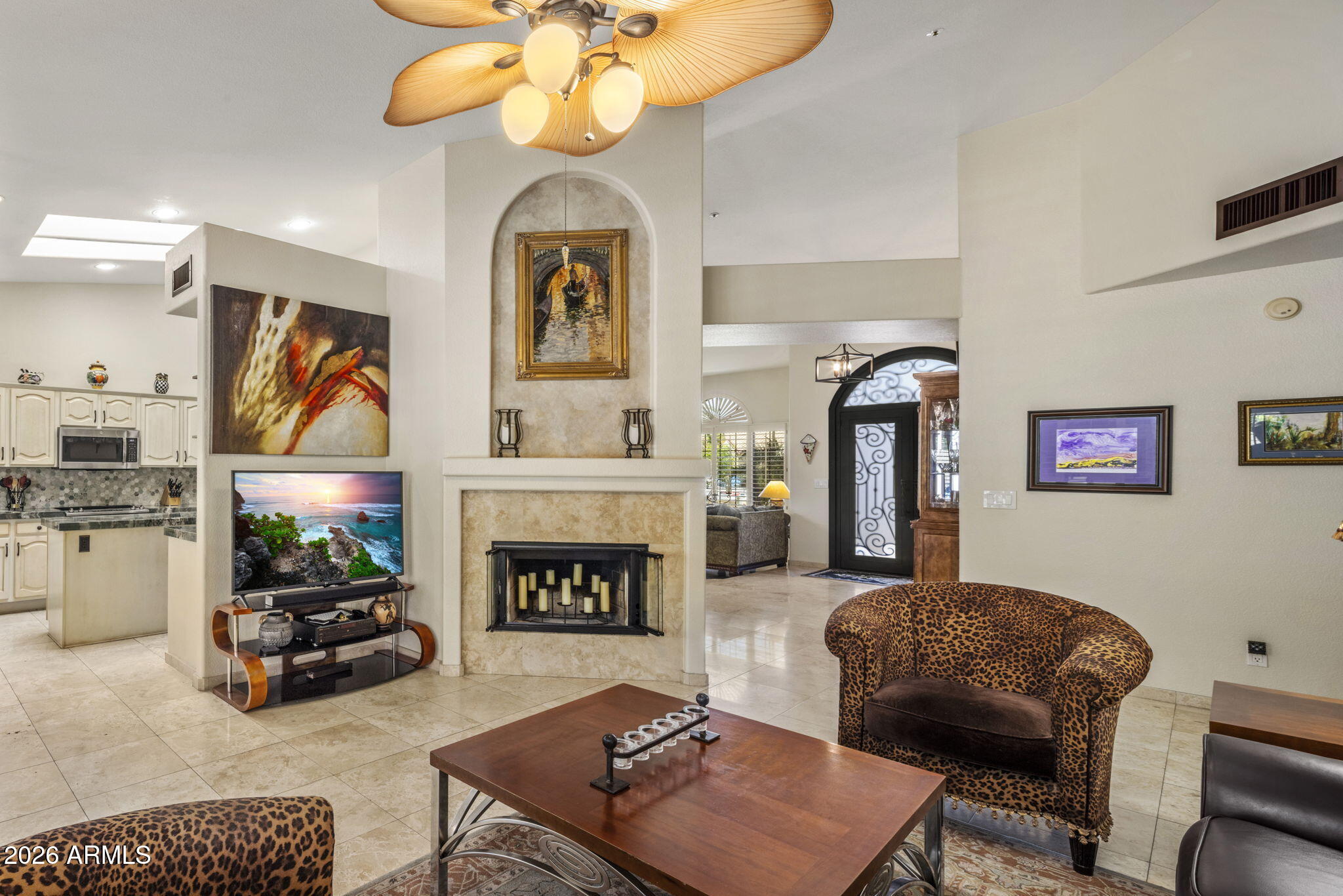 Living room with a stone fireplace, leopard-print chairs, and an open kitchen.