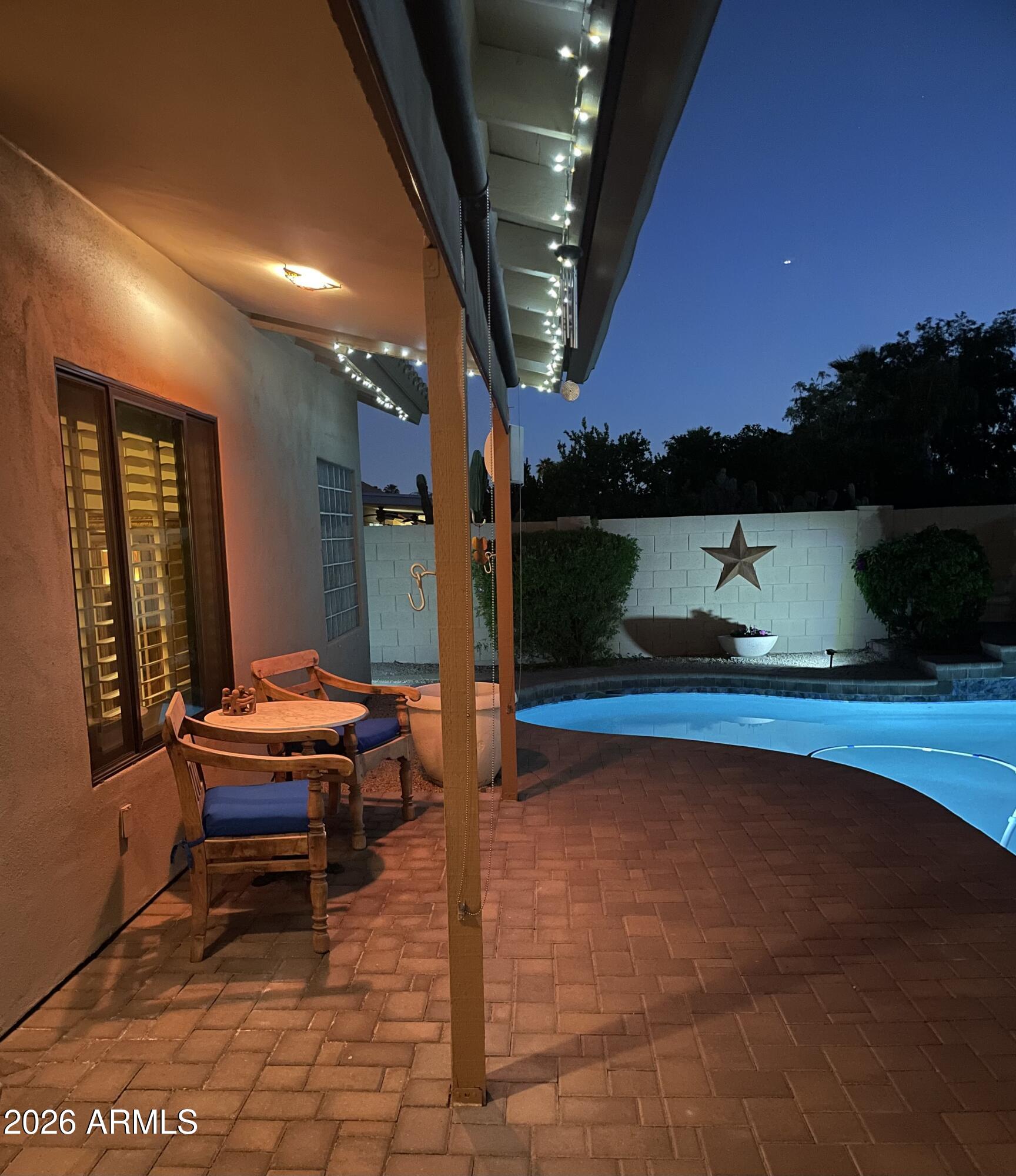 Backyard pool and brick patio at night, with covered seating and a star on the garden wall.