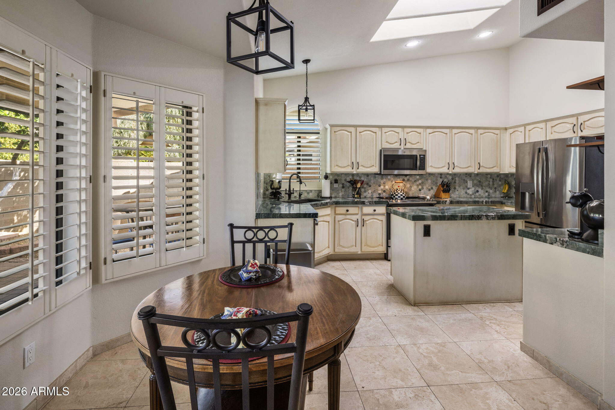 Kitchen with green stone counters, cream cabinets, stainless appliances, and plantation shutters.