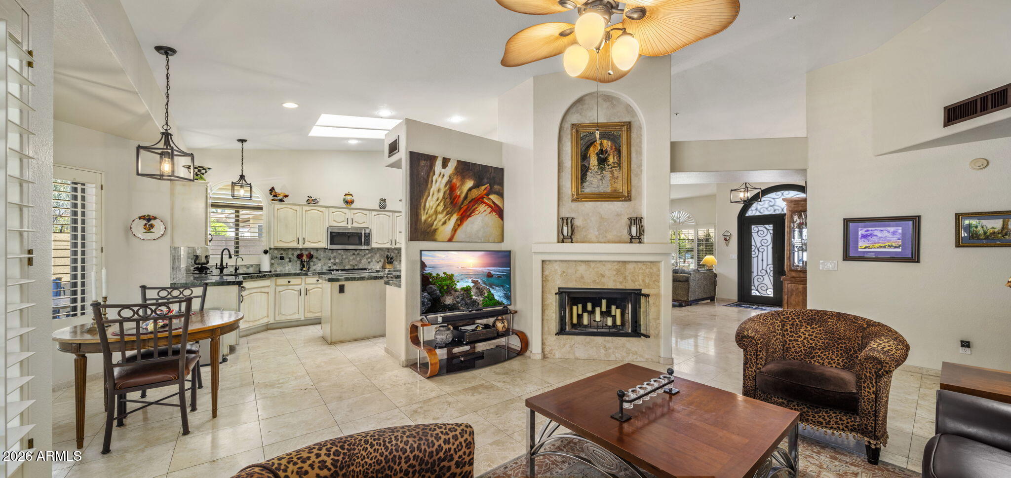 Open living room and kitchen with a stone fireplace, dining table, and leaf-shaped ceiling fan.