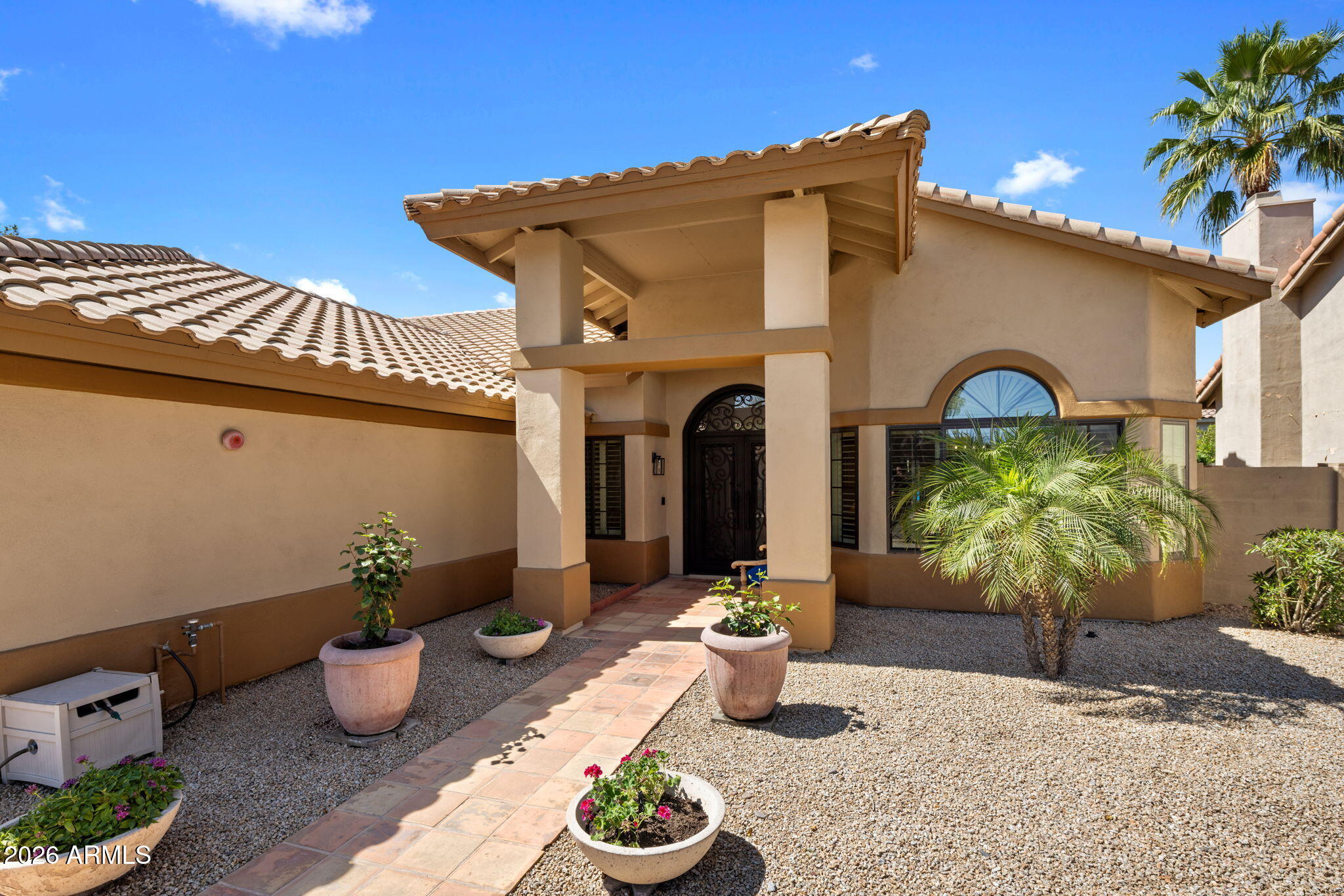 Tan stucco home with a tiled roof, covered entry, arched window, and gravel landscaping.