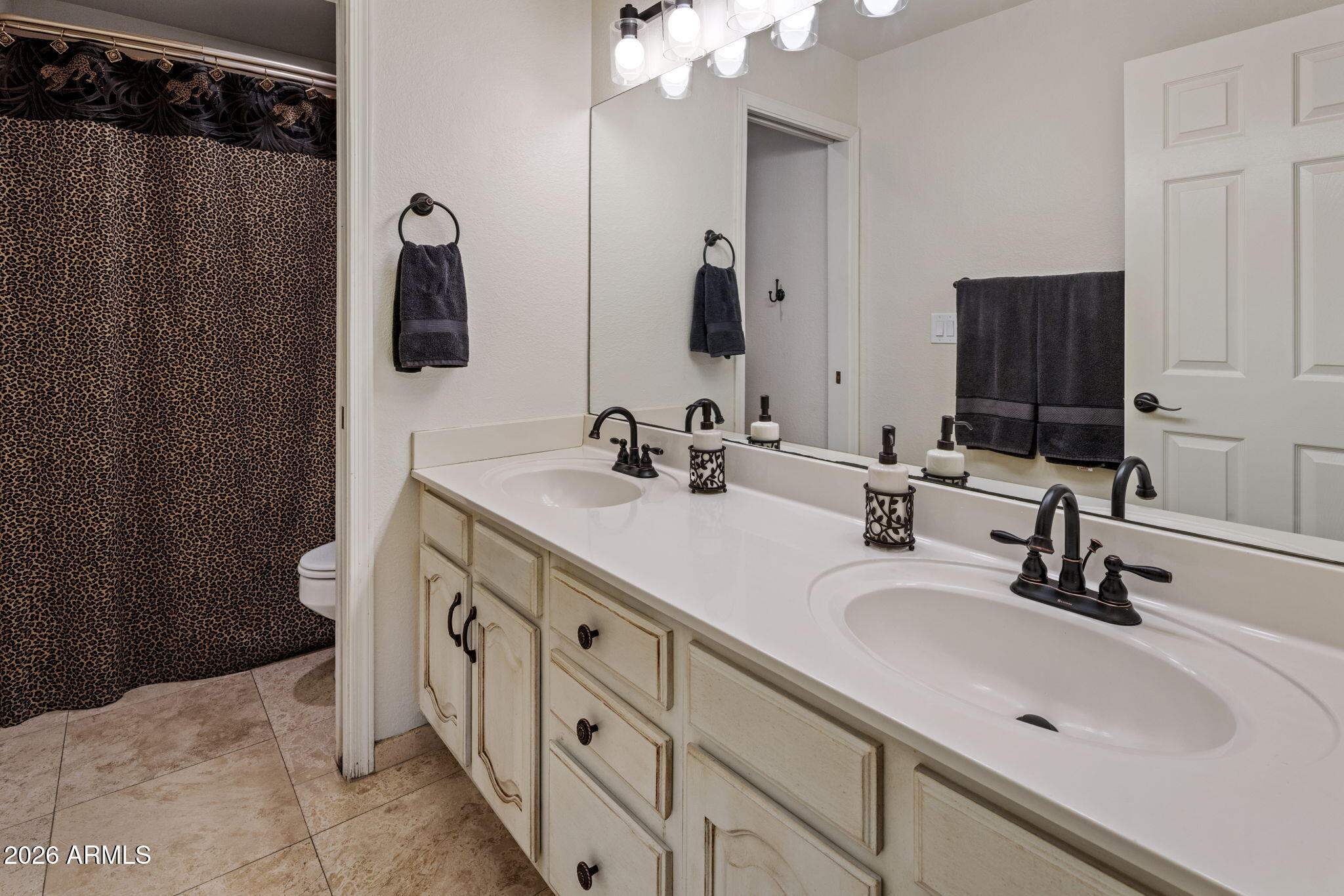 Bathroom with a cream double vanity, black faucets, large mirror, and leopard-print shower curtain.