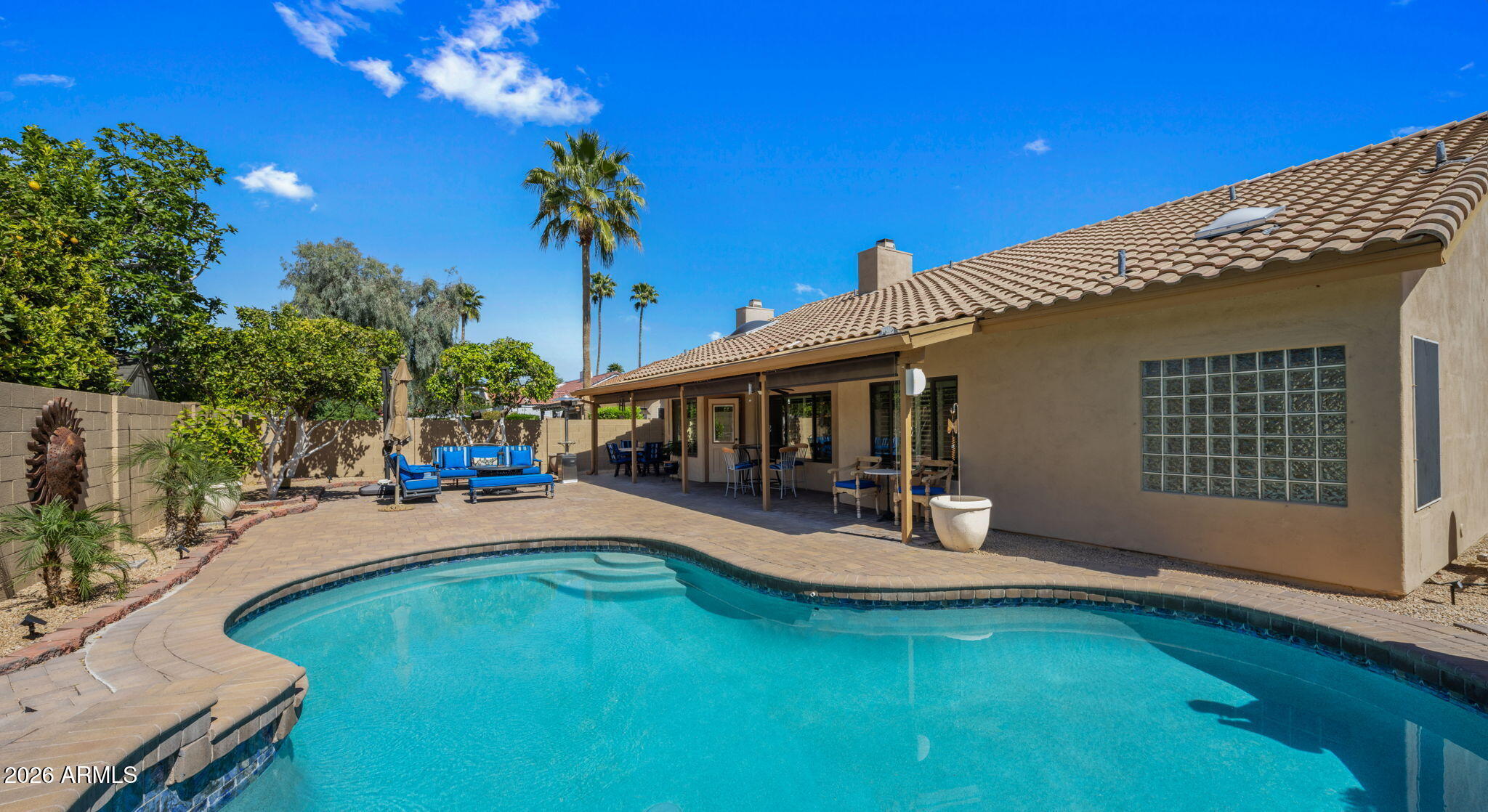 Backyard pool beside a tan stucco home with a covered patio and palm trees.