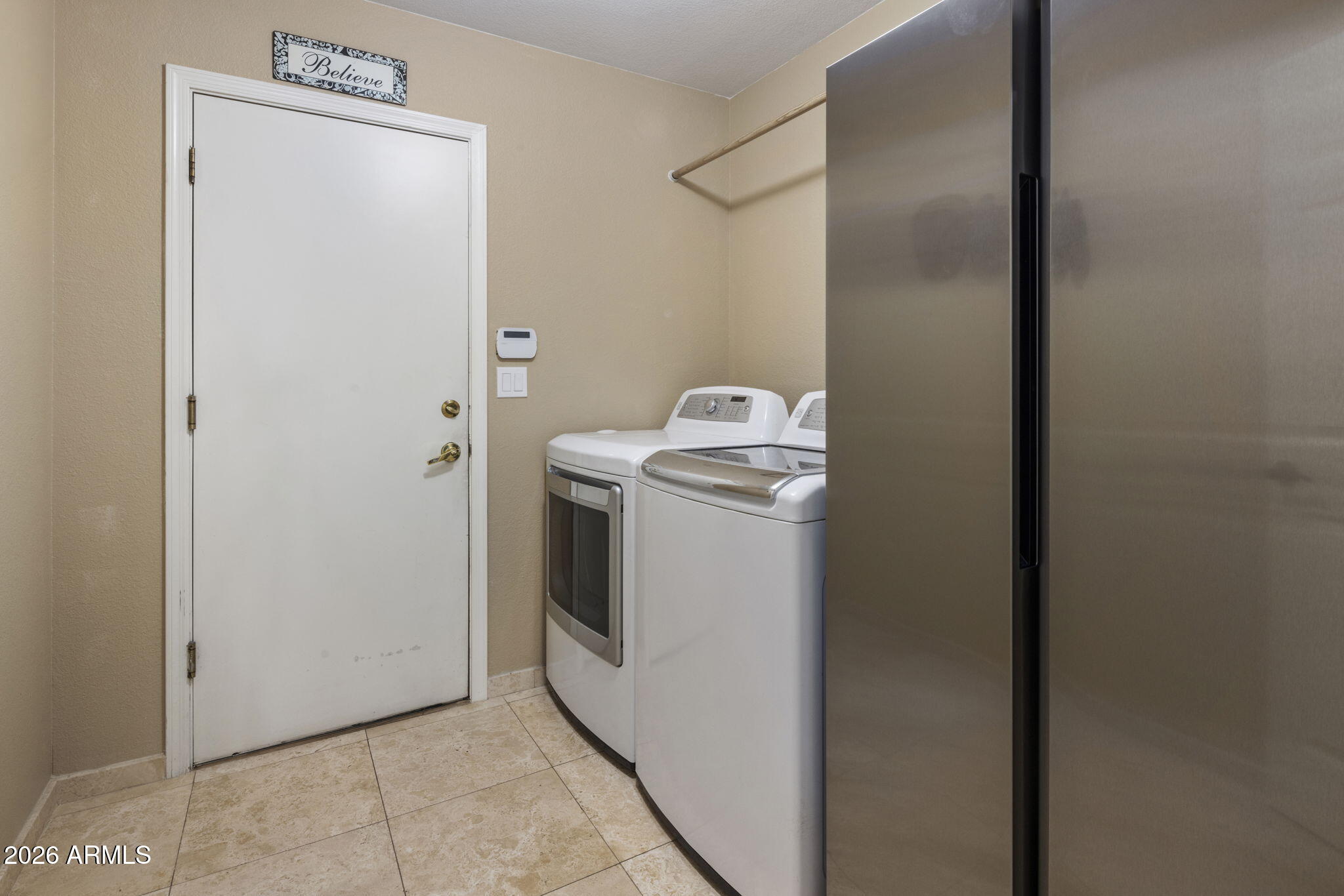 Laundry room with a washer and dryer beside a tall stainless-steel refrigerator.