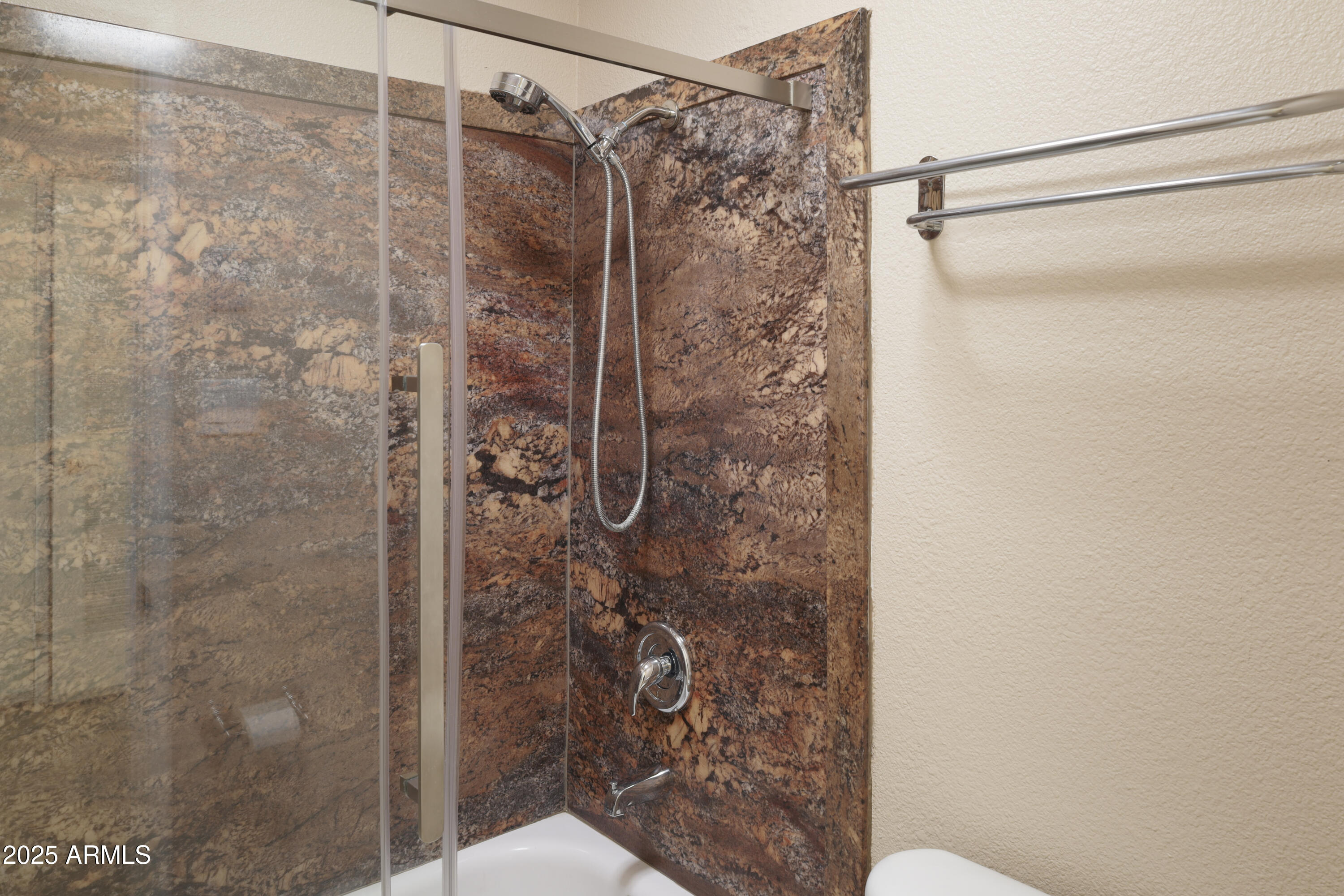 Bathroom shower with patterned stone walls, glass enclosure, and handheld showerhead.