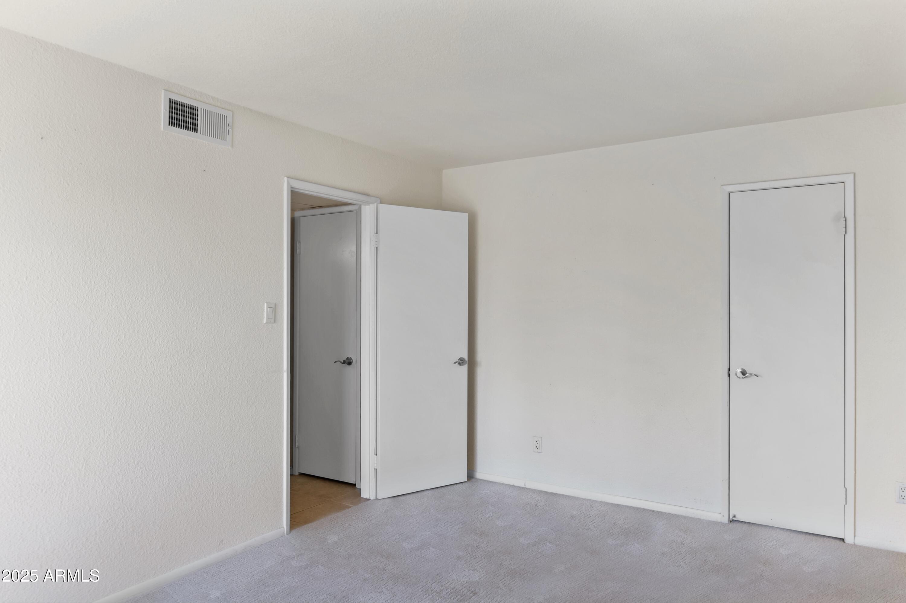Empty carpeted room with two doors and a ceiling air vent.