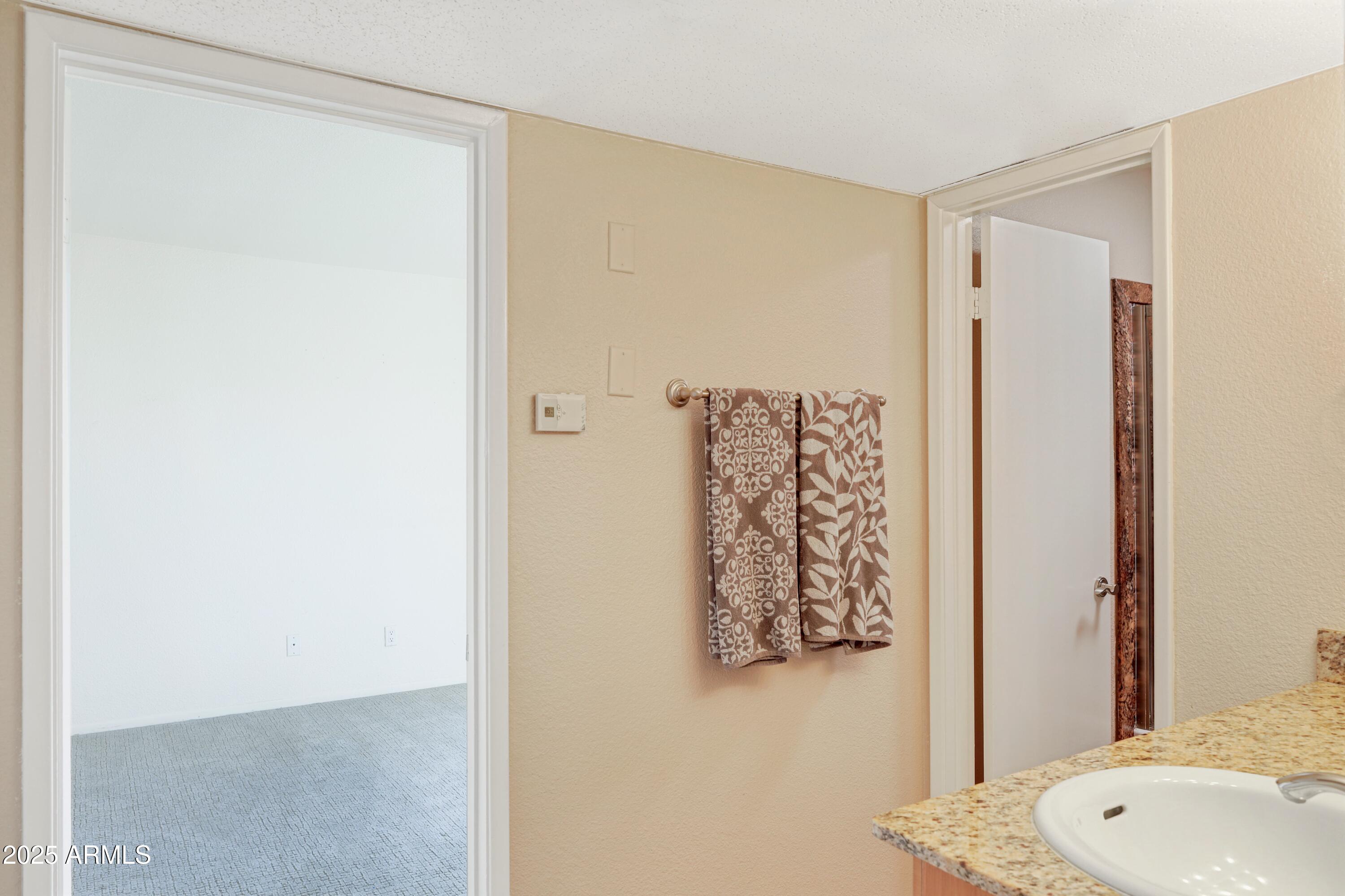 Bathroom vanity with a granite counter, patterned towels, and an open doorway to a carpeted room.