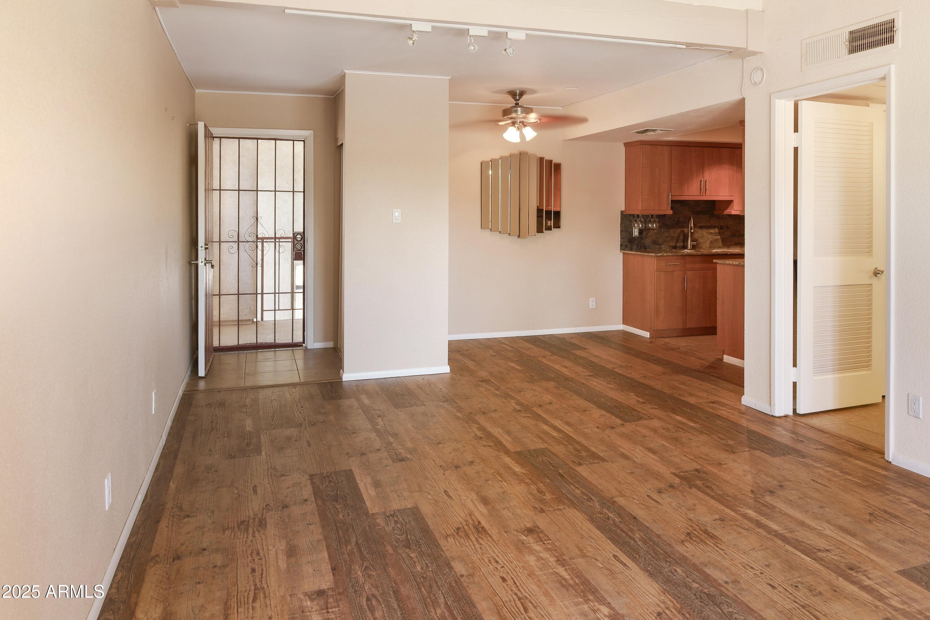 Unfurnished living area with wood-look flooring, ceiling fan, and open kitchen.