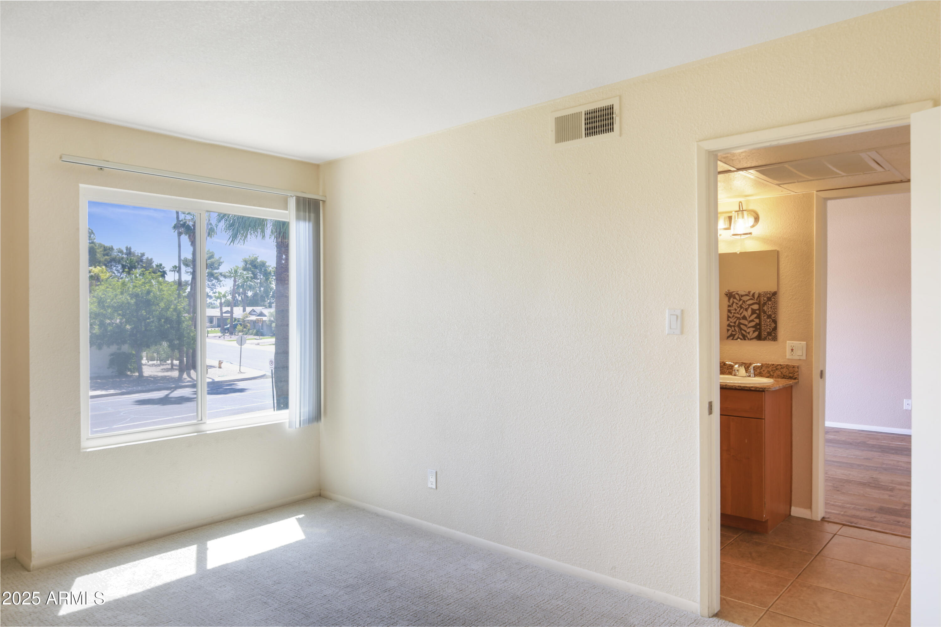 Empty carpeted room with a large street-facing window and an open doorway to a bathroom.