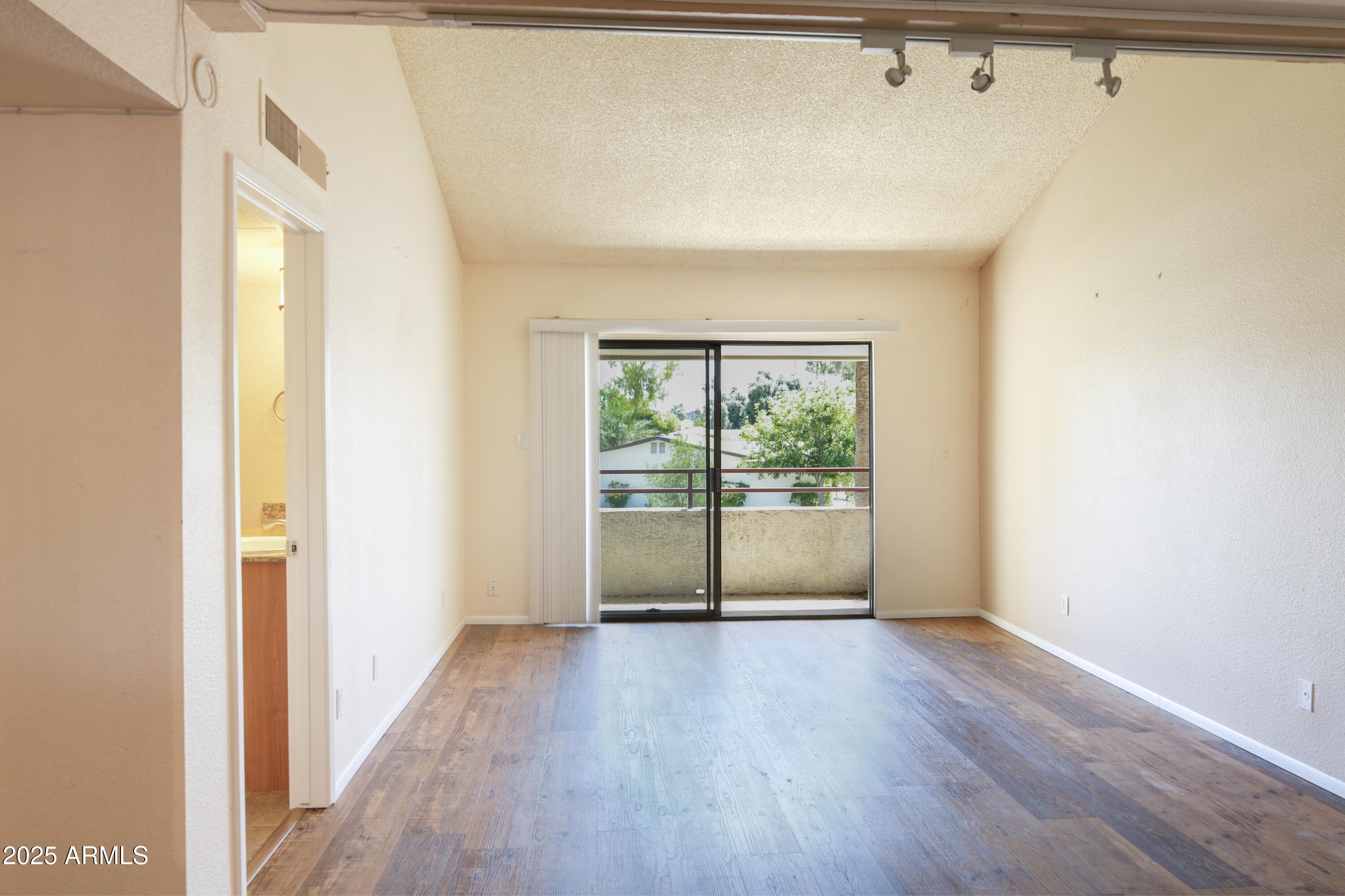 Vacant room with wood-look floors and sliding doors opening to a balcony.