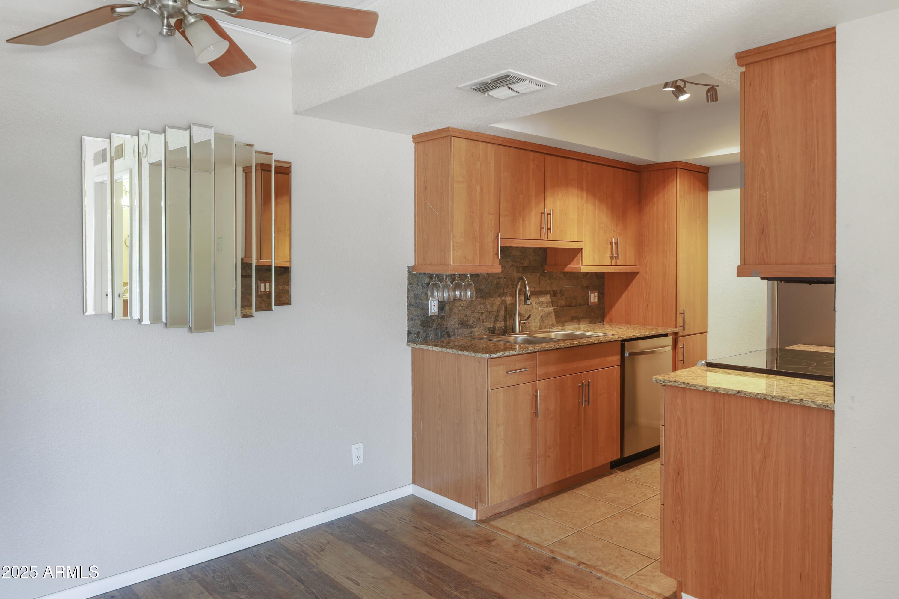 Kitchen with warm wood cabinetry, granite counters, stone backsplash, and a stainless steel dishwasher.