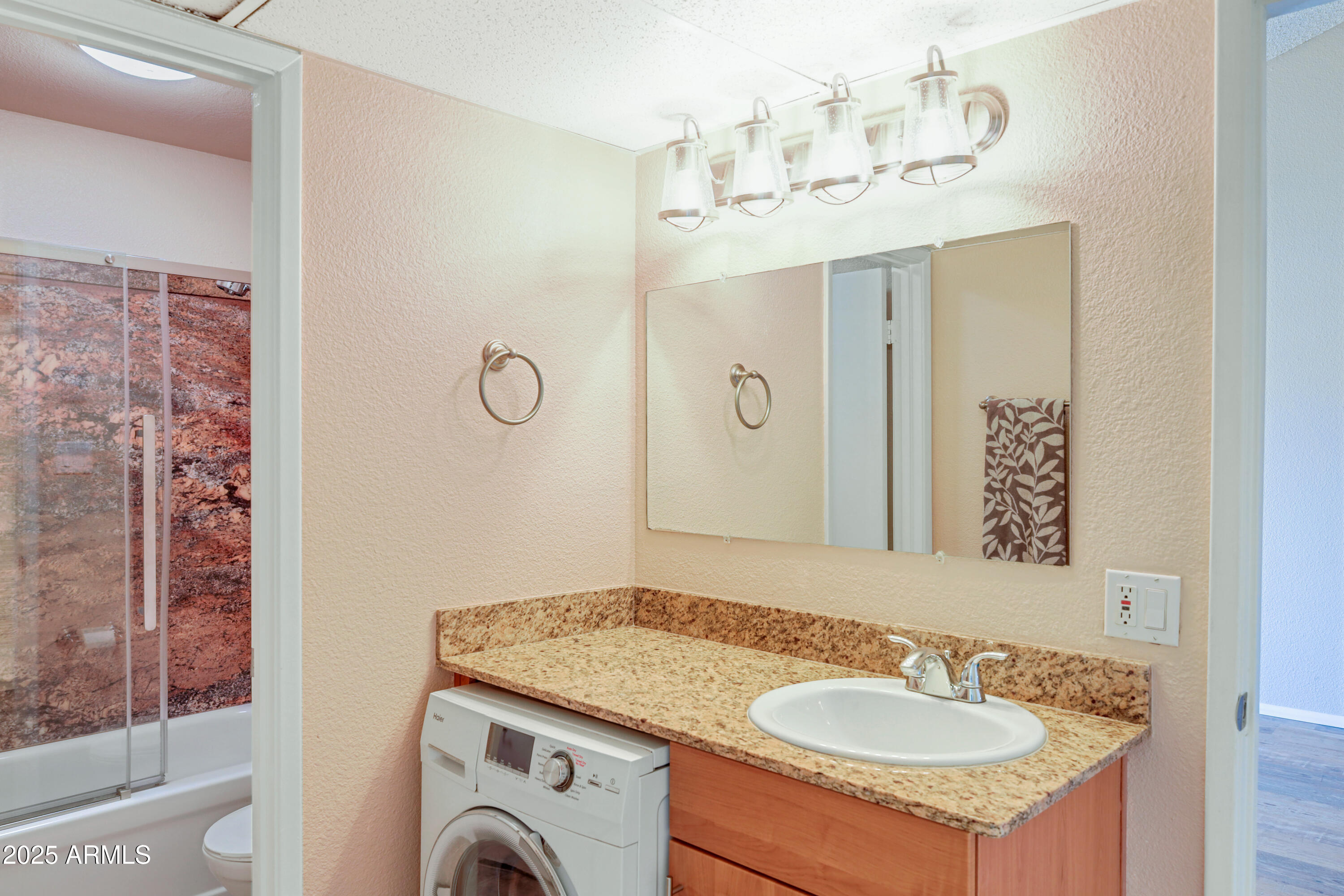 Bathroom vanity with an under-counter washer and a glass-enclosed tub and shower.