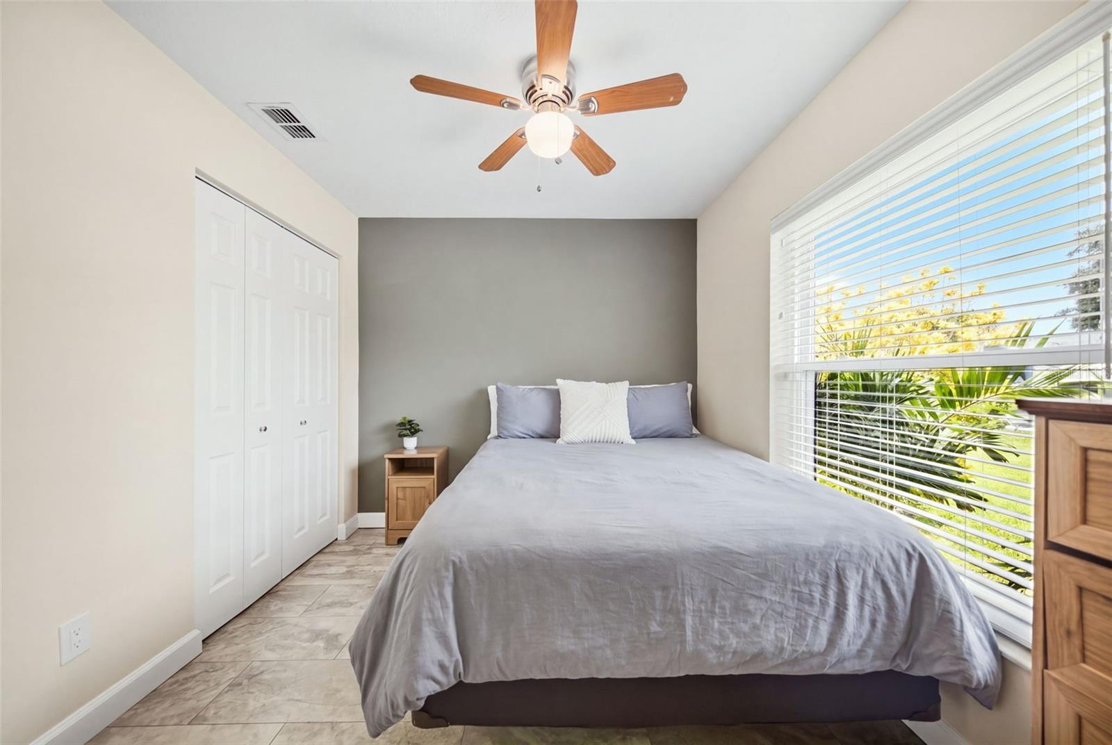 Bedroom with a gray bed, dark accent wall, and large window overlooking greenery.