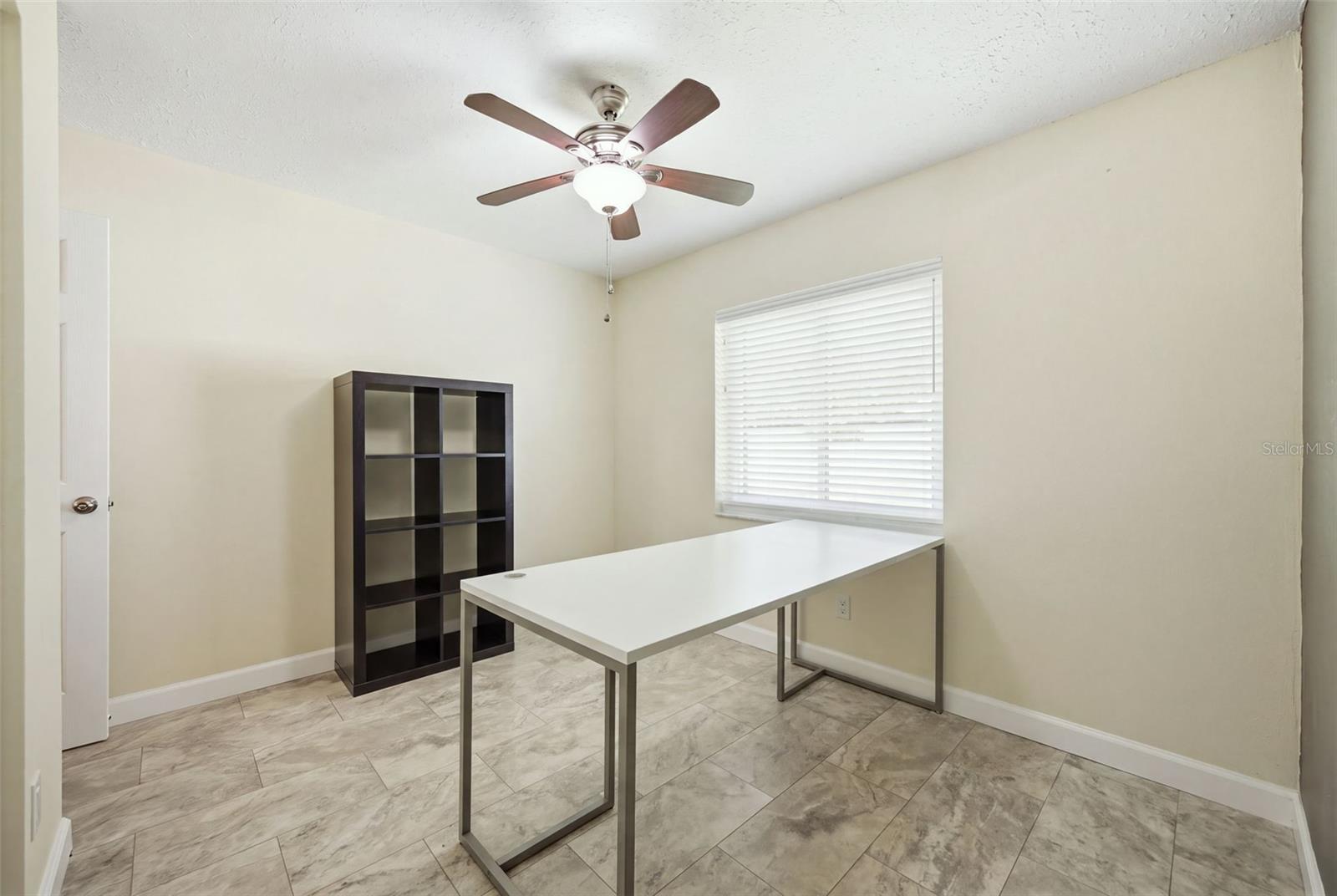 Office with a white desk, dark shelving, tiled floor, and window with blinds.